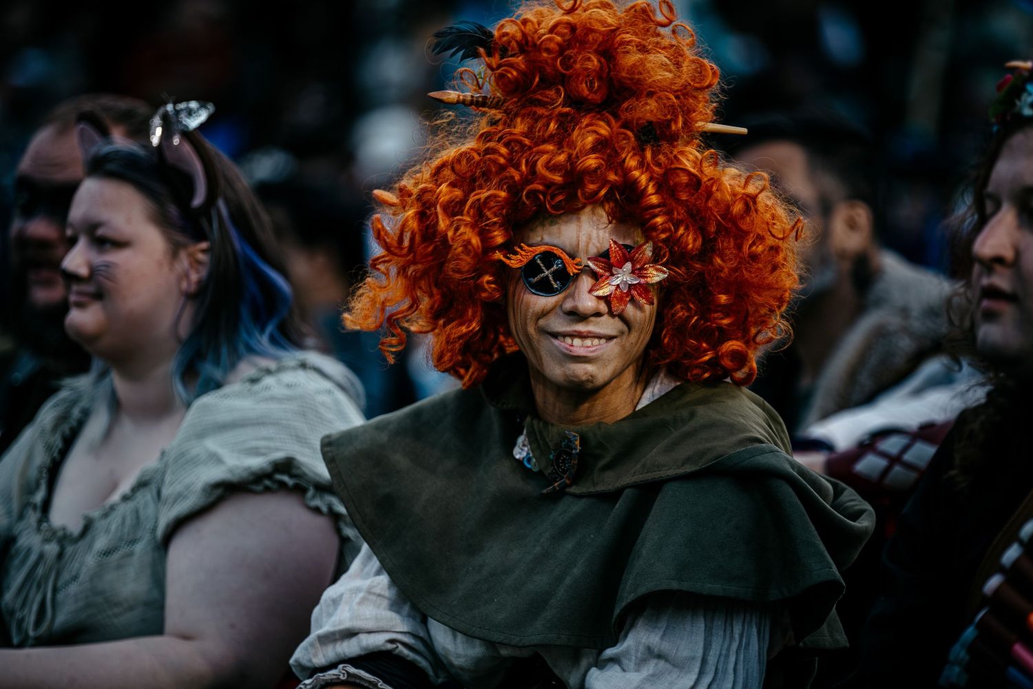 Person in orange curly wig, fantasy costume, and decorative glasses at a Renaissance faire event.