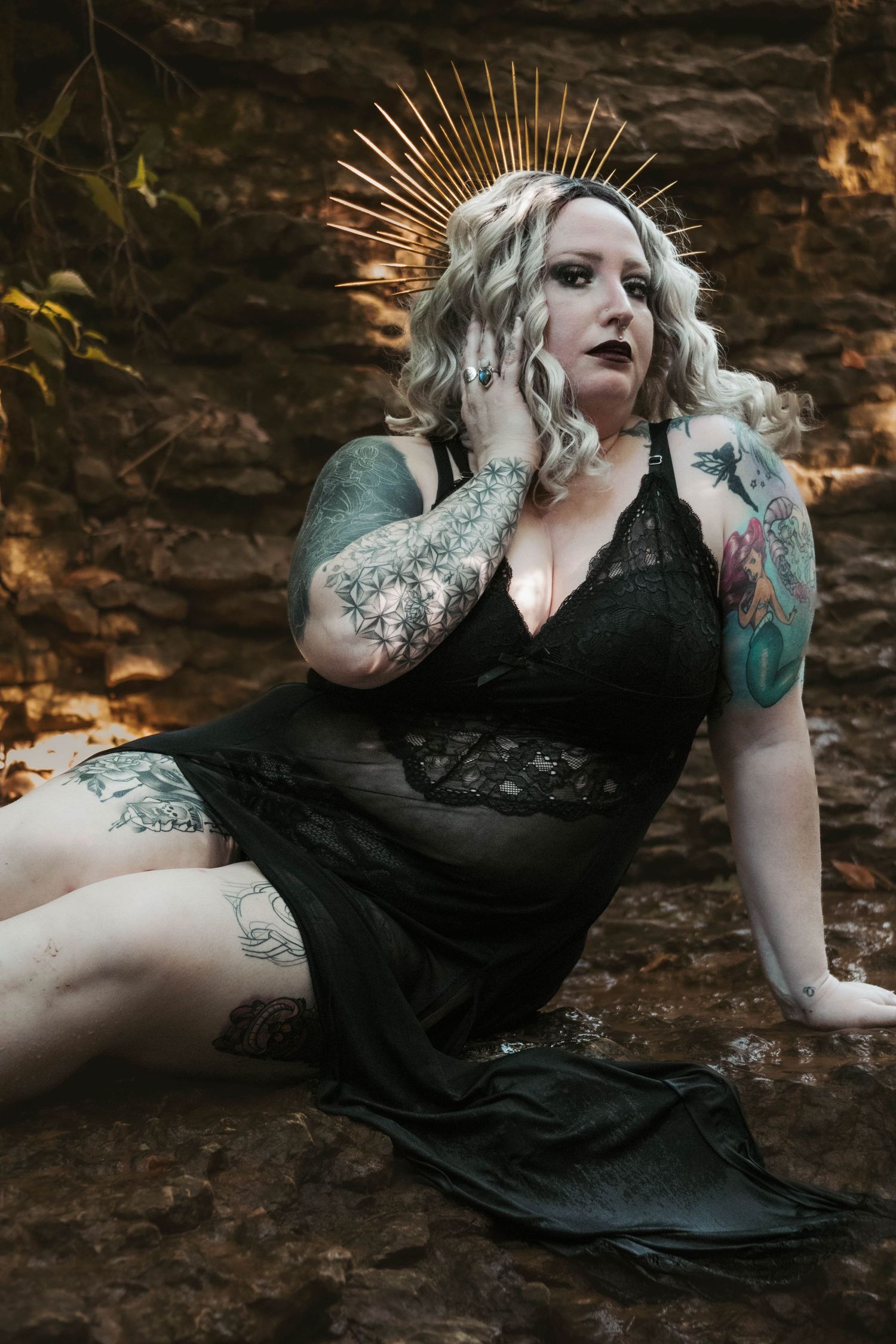 Gothic glamour portrait with spiked crown, black lace dress, and dramatic rock wall background.