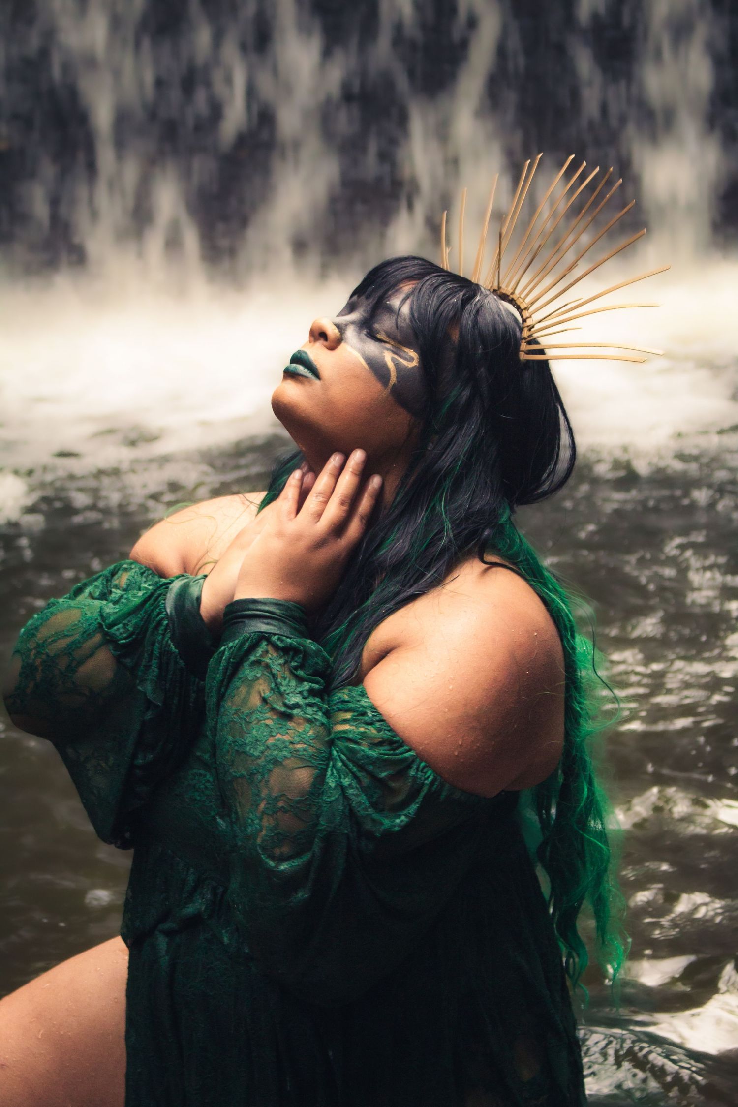 A dramatic portrait of someone in emerald green lace with gold accessories against a textured background.