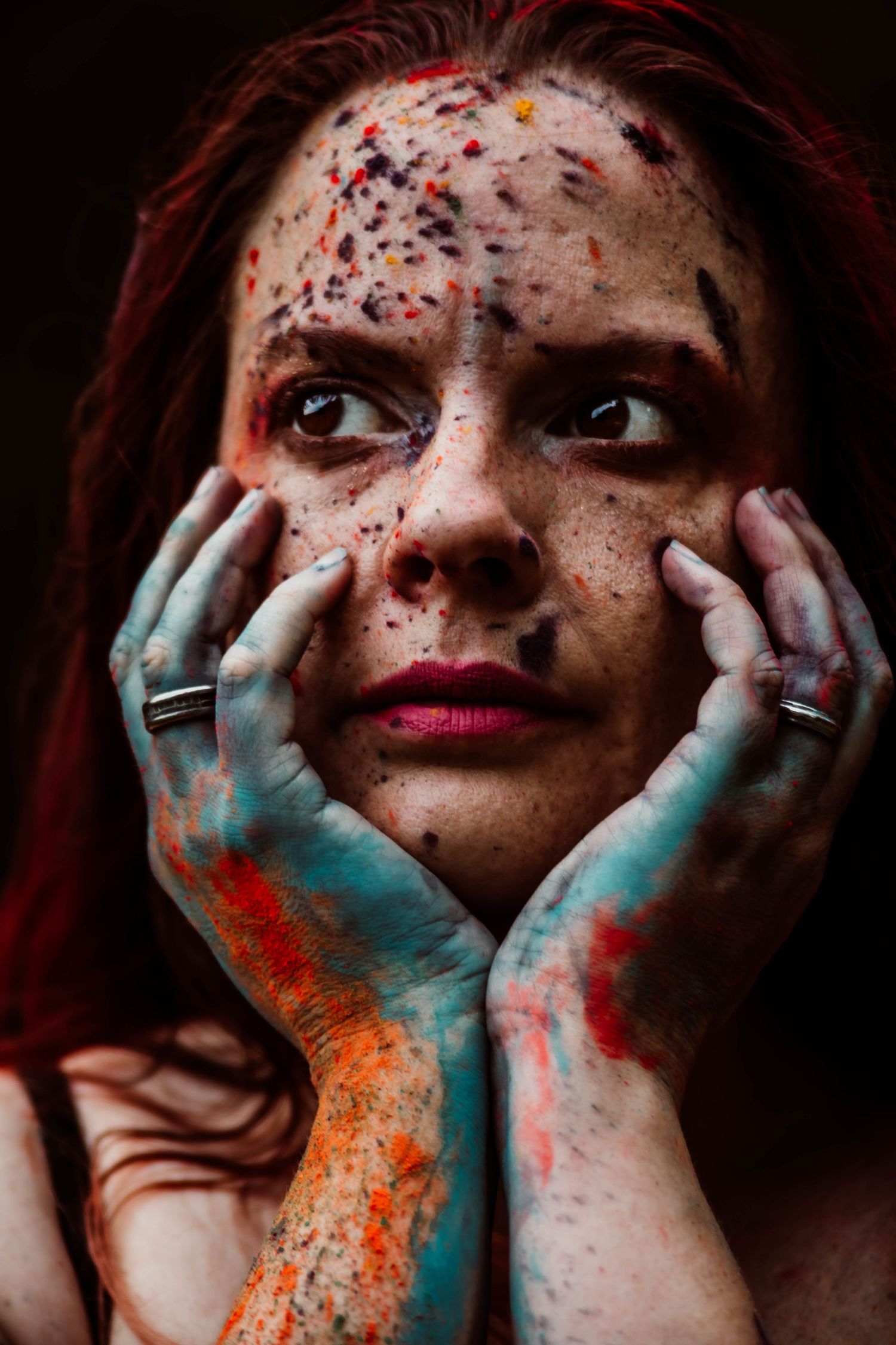 Artistic portrait with colorful powder makeup and paint-stained hands framing the face.