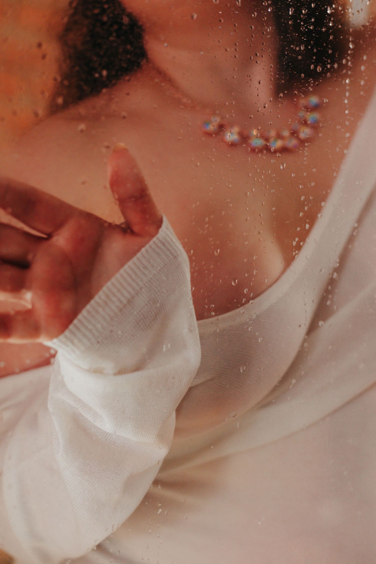 Closeup of white fabric through rain-spotted glass creating dreamy texture.