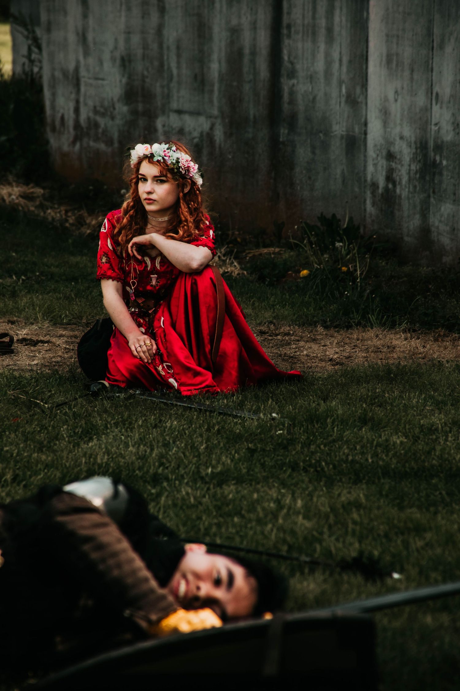 Artistic portrait featuring red dress against dark concrete wall in moody lighting.
