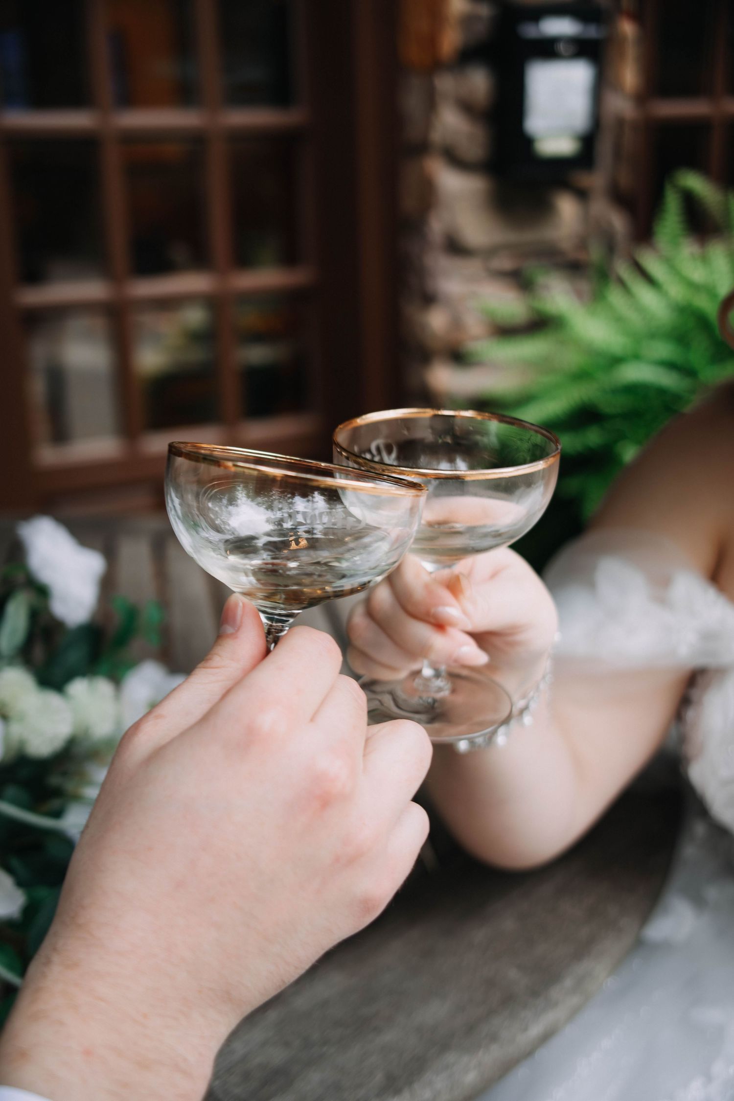 Four sequential images show hands holding coupe glasses filled with a pink cocktail against a rustic backdrop.