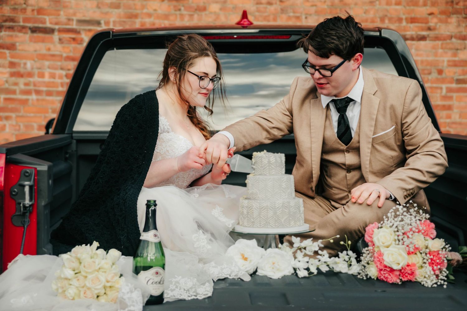 A couple in wedding attire leans across a table decorated with red and white floral arrangements.