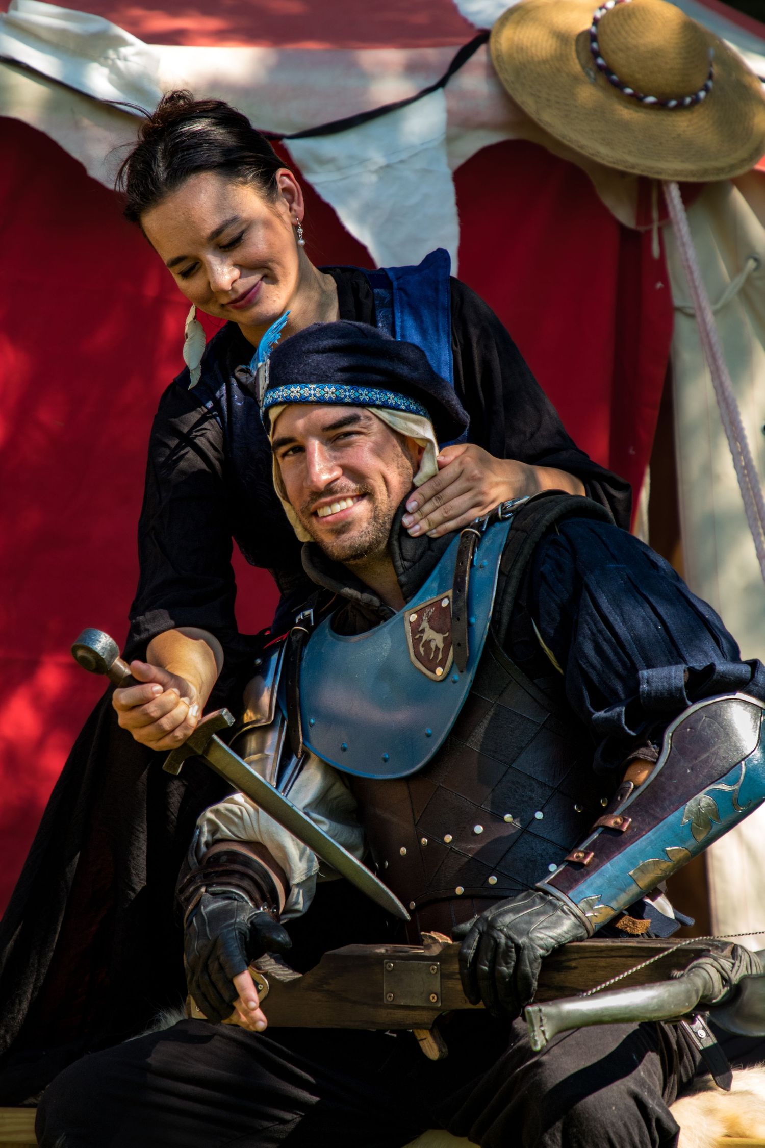 Medieval performers in black leather armor and chainmail share a lighthearted moment during a historical reenactment.