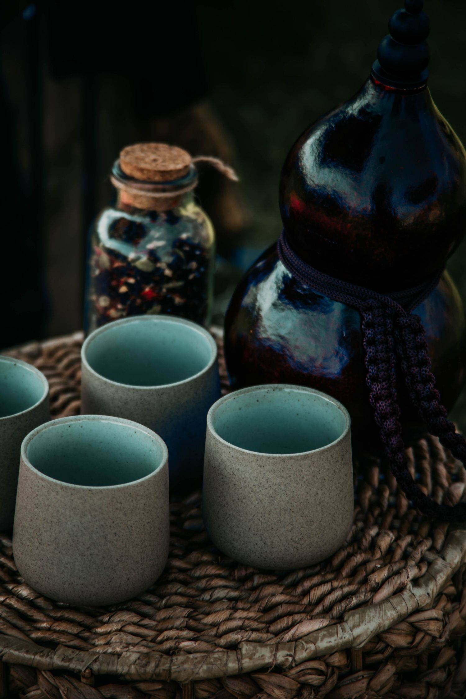 Rustic ceramic cups with turquoise interiors displayed alongside dark bottle and spice jar on textured burlap surface.