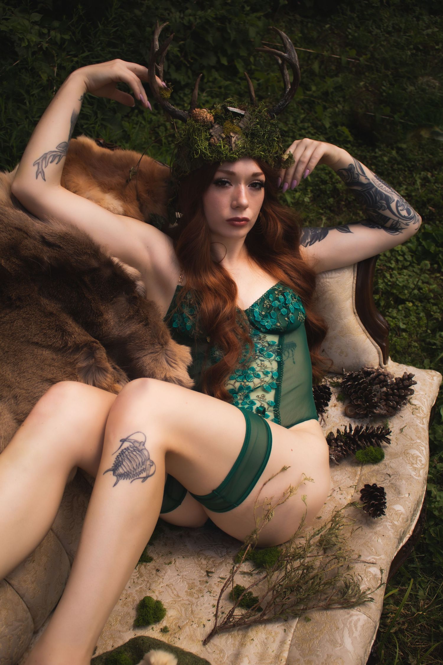Fantasy forest photoshoot with antlers and green corset on rustic backdrop among leaves and moss.