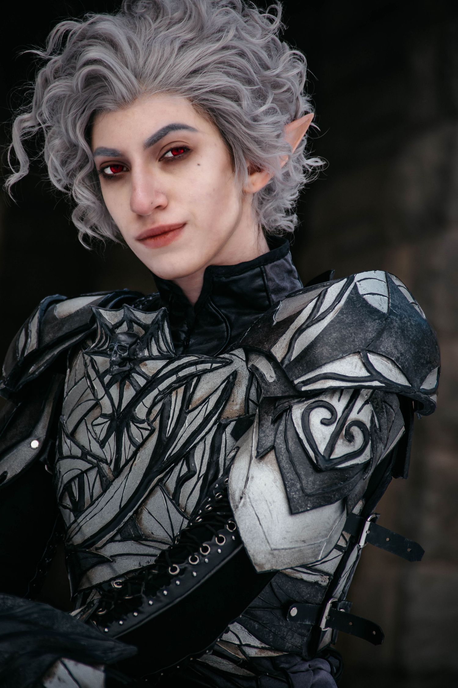 Fantasy cosplay character wearing ornate silver and black armor with curly grey hair and pointed elf ears.