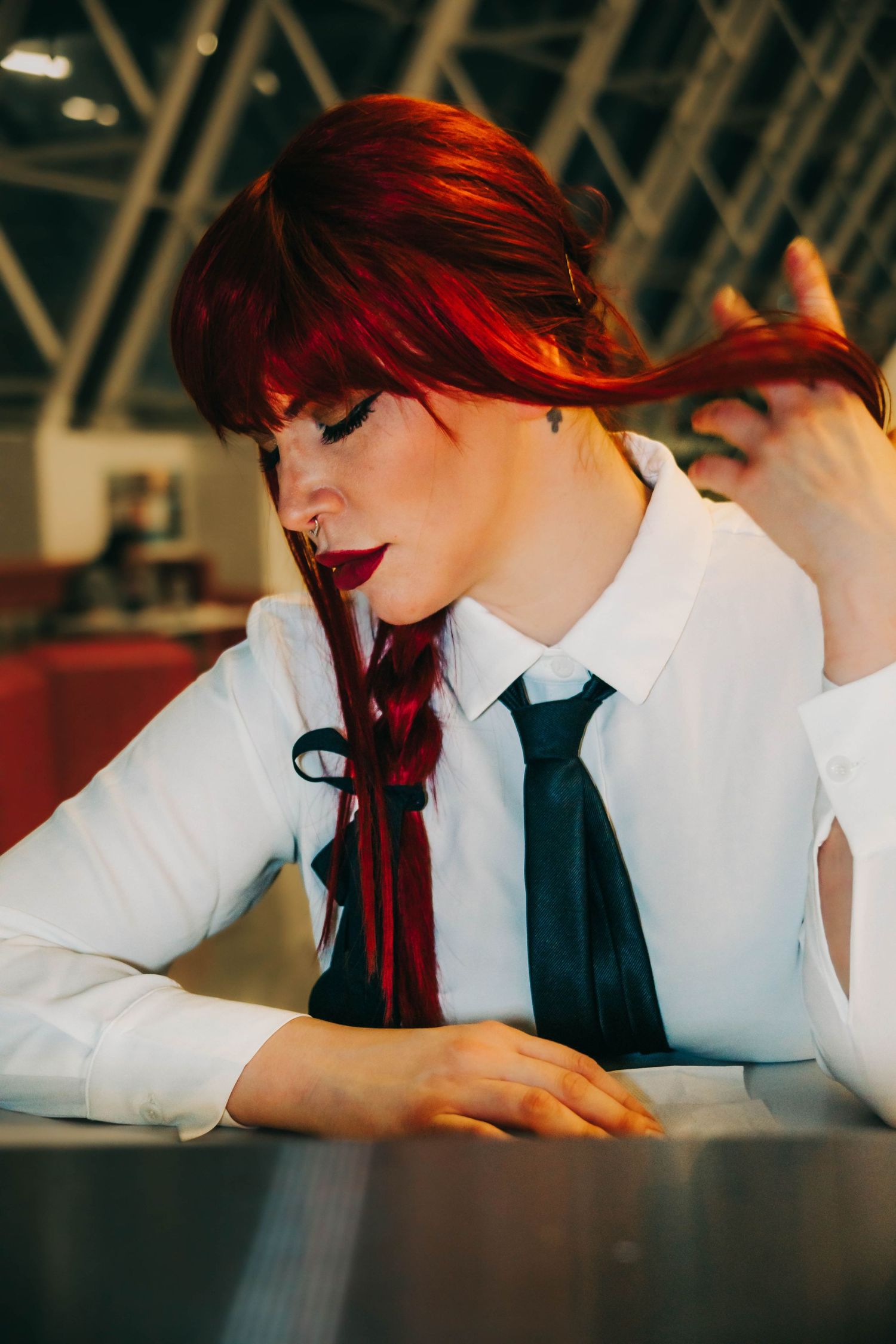A student with vibrant red hair rests their head on a desk while studying in a classroom setting.