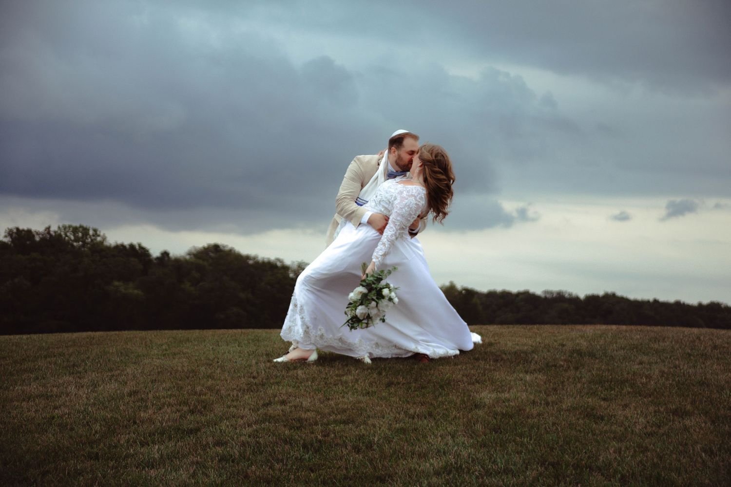Two figures in white dresses dance across a grassy hilltop against a dramatic stormy sky.