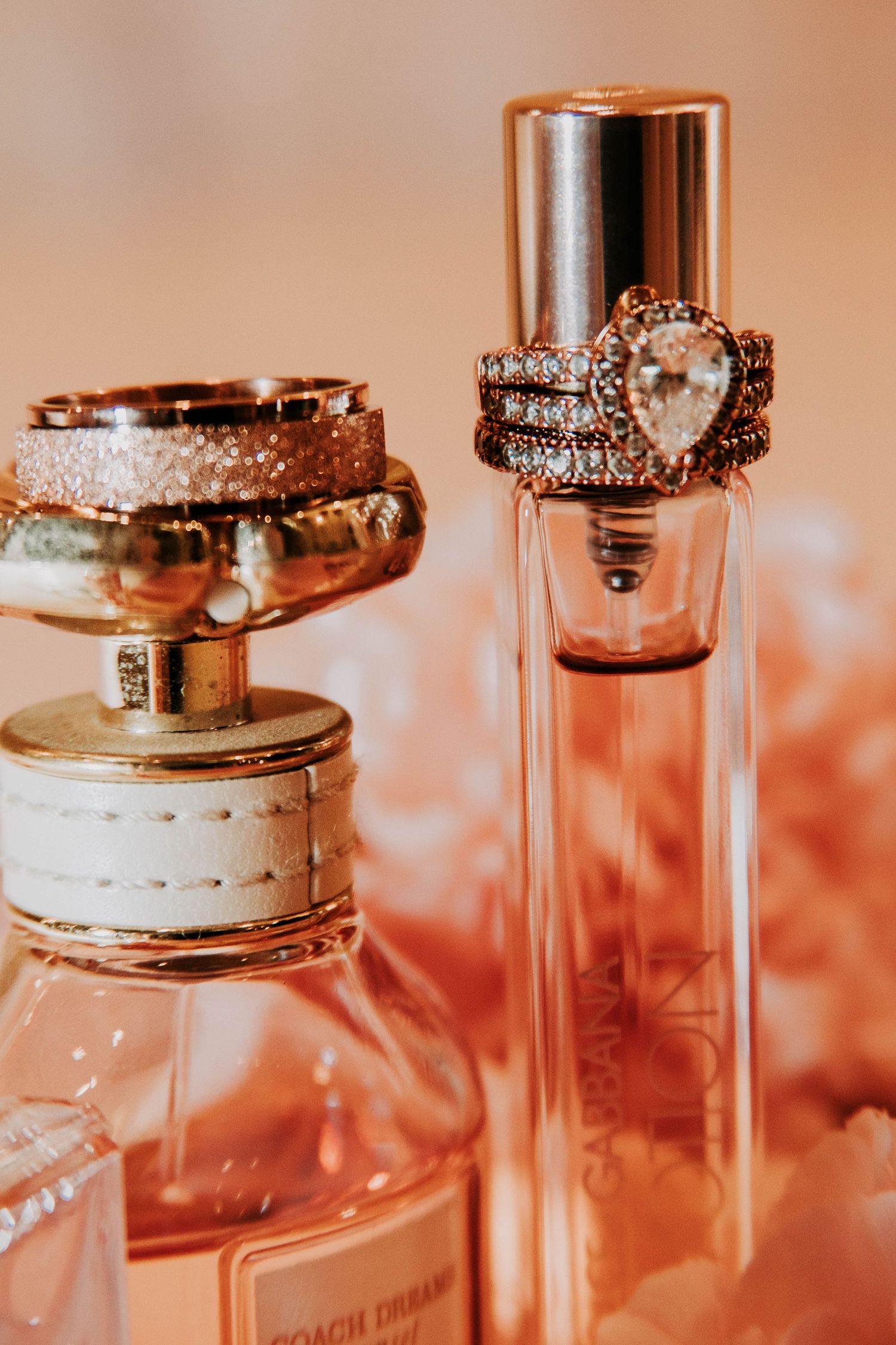 Elegant wedding rings displayed in glass jars with warm lighting and romantic peach-colored background.