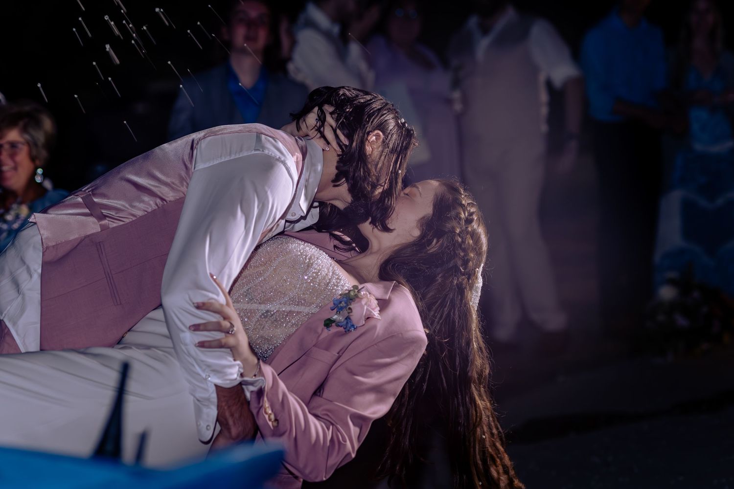 Couple sharing a romantic kiss in the rain at an outdoor evening wedding reception.