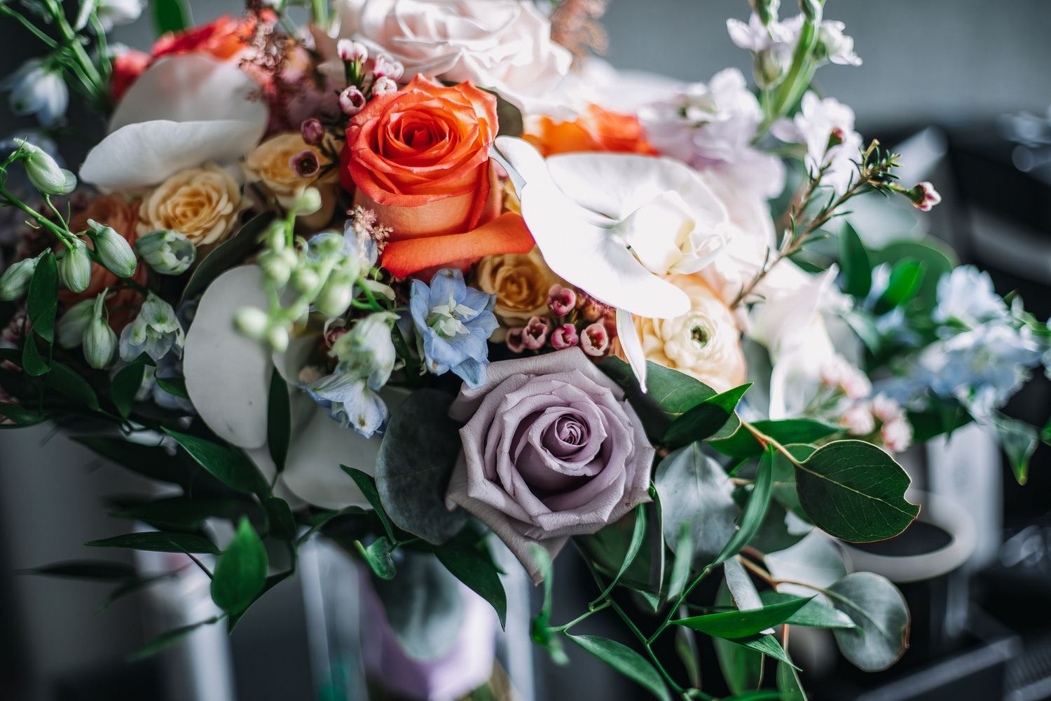 Elegant wedding bouquet featuring orange roses, lavender roses, white calla lilies, and eucalyptus greenery.