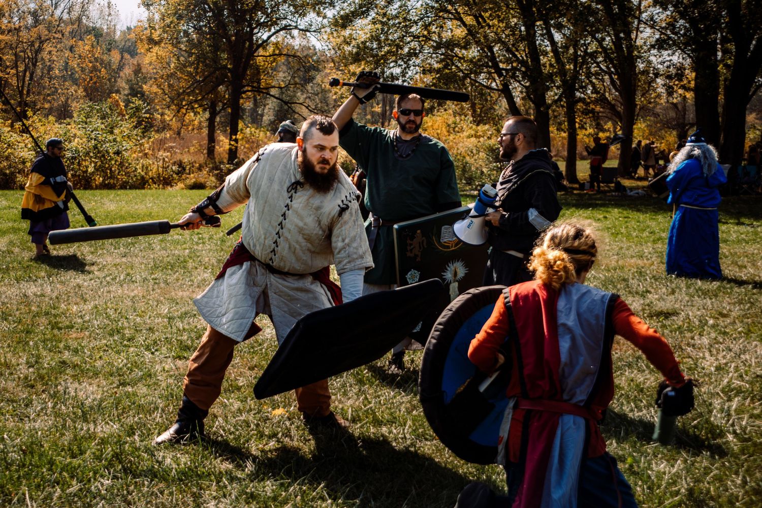 Medieval combat reenactors engage in battle on autumn field.
