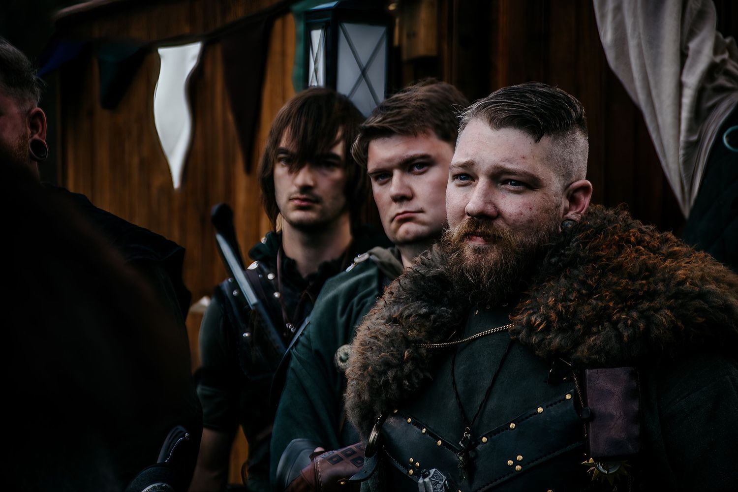 Three men in medieval Viking costumes stand together at a historical reenactment event, wearing fur and leather armor.