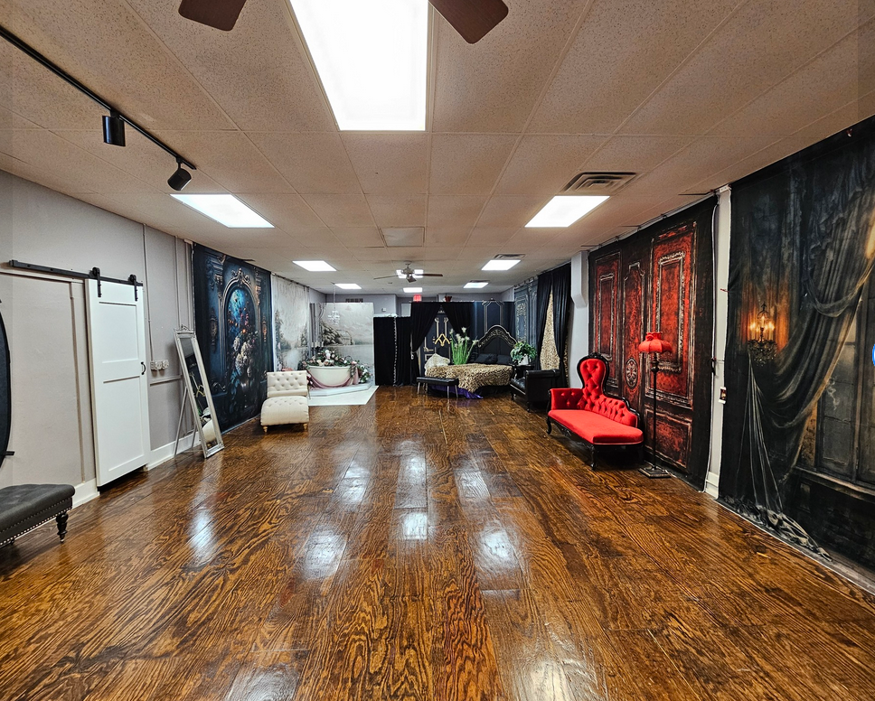A long empty dance studio with polished hardwood floors, mirrored walls, and fluorescent lighting in the ceiling.