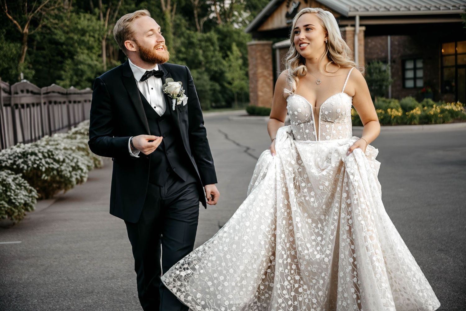 A couple shares a romantic moment in formal wedding attire surrounded by greenery outdoors.