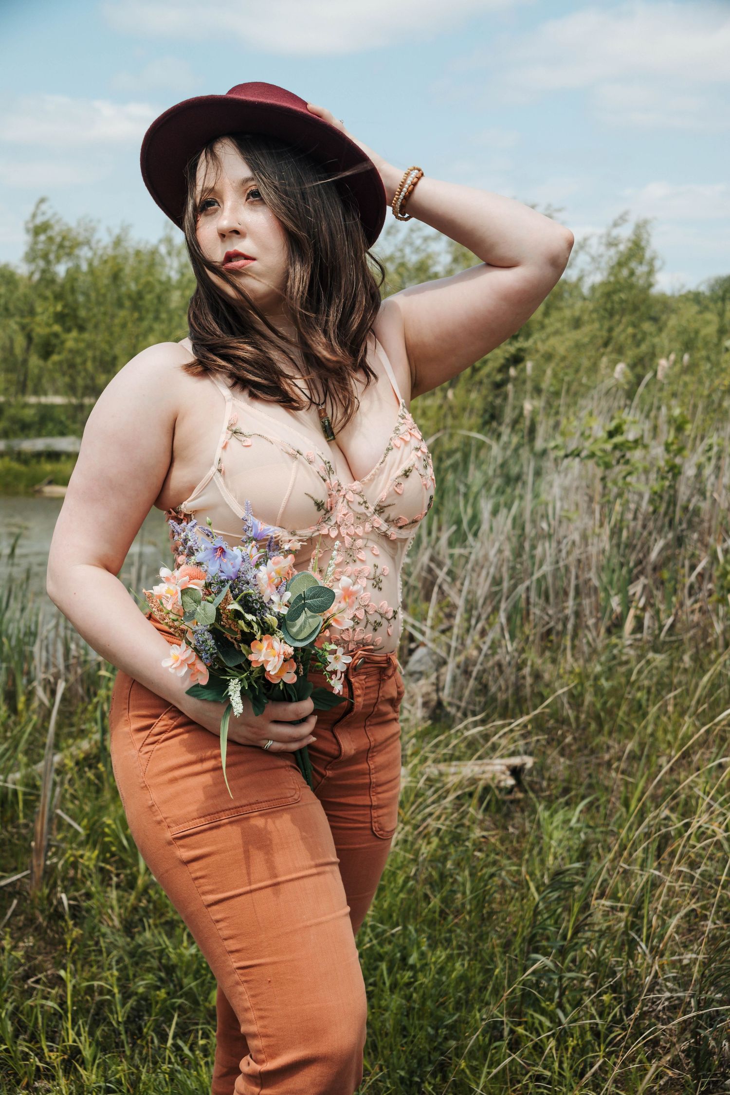 A person in a peach dress and brown skirt poses in a wildflower meadow holding a bouquet of flowers.