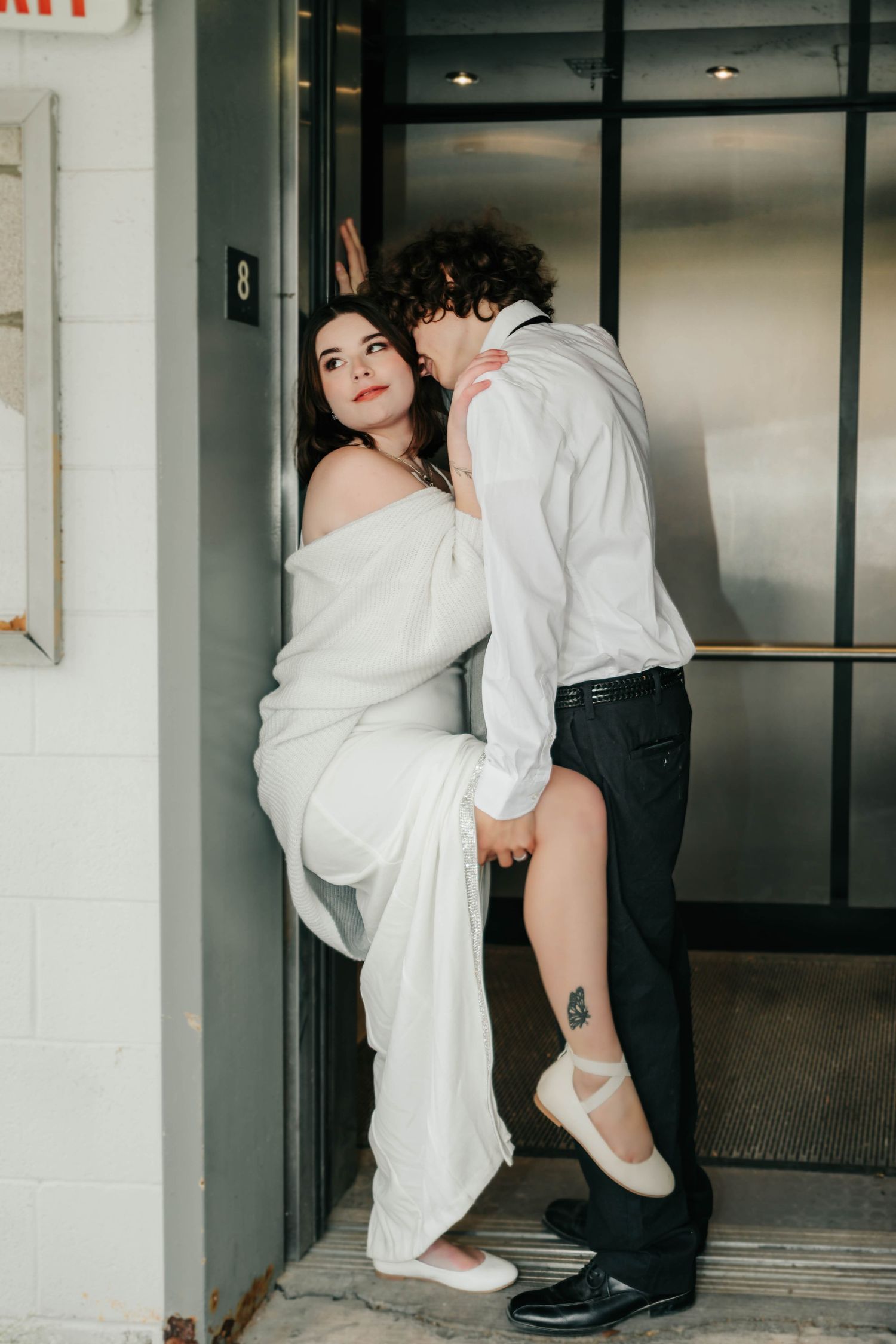A romantic moment between a couple in formal wear near an elevator entrance.