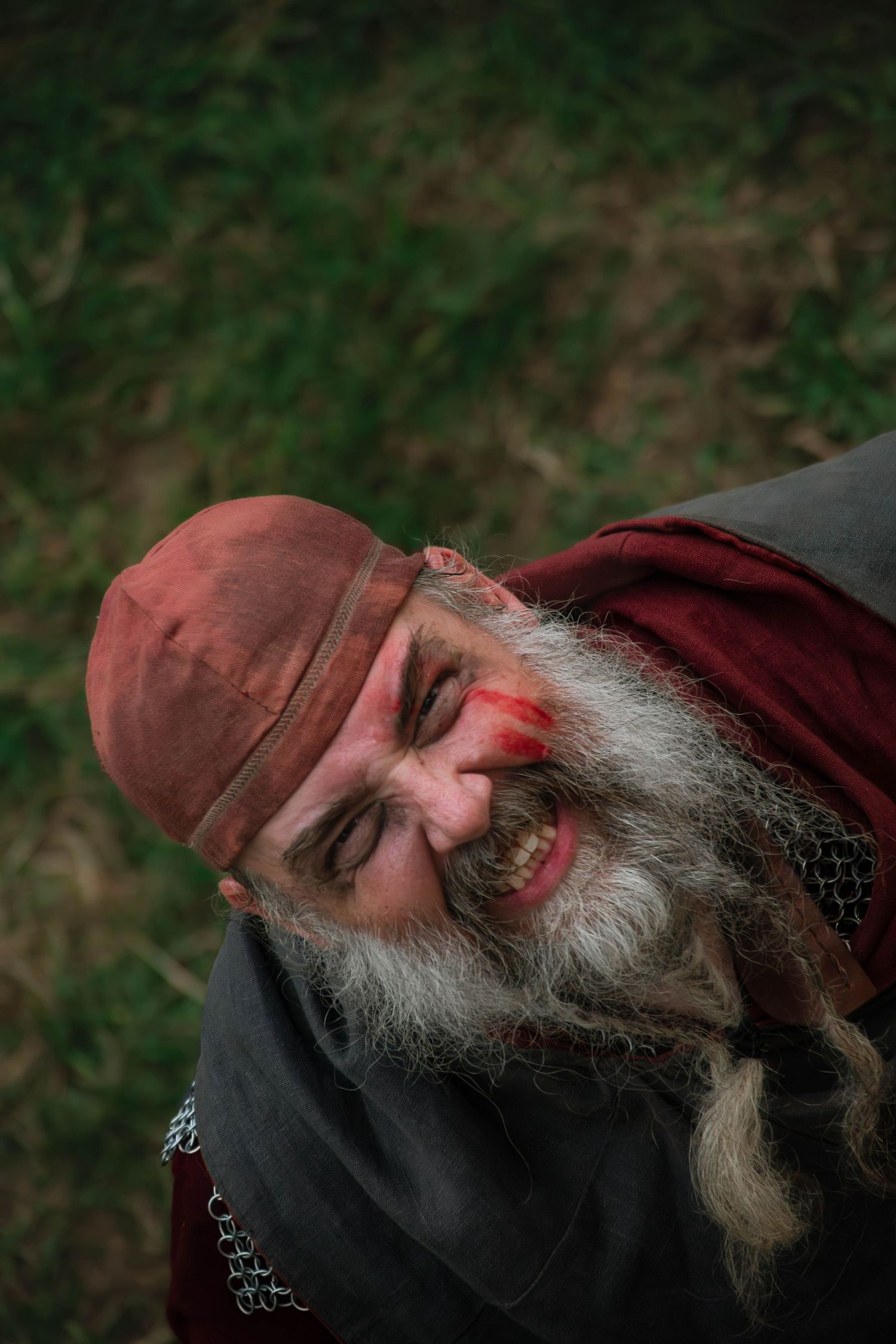 Person in medieval garb with long beard lying on grass during reenactment event.