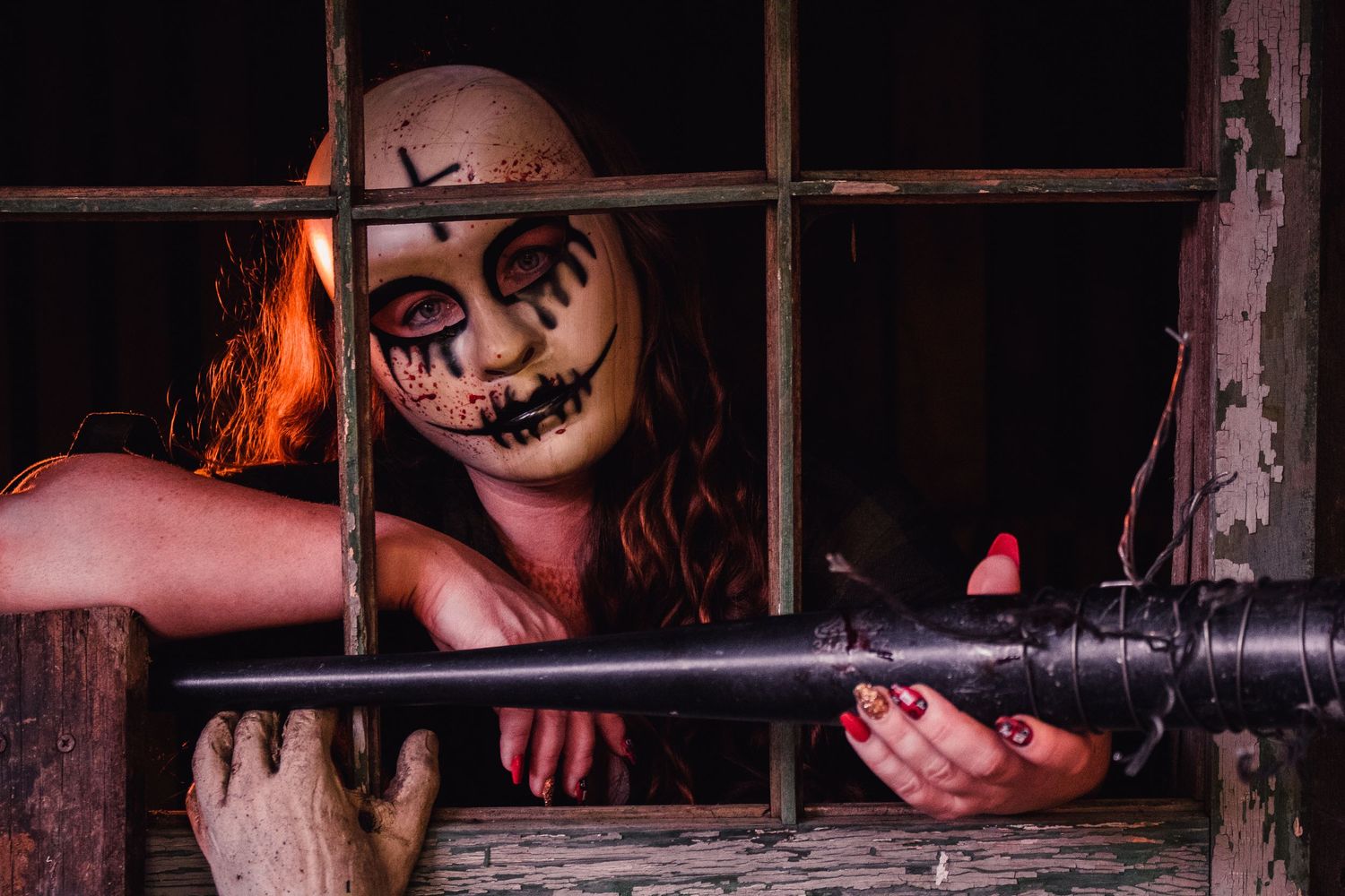 A haunting masked figure peers through wooden slats in dim lighting.