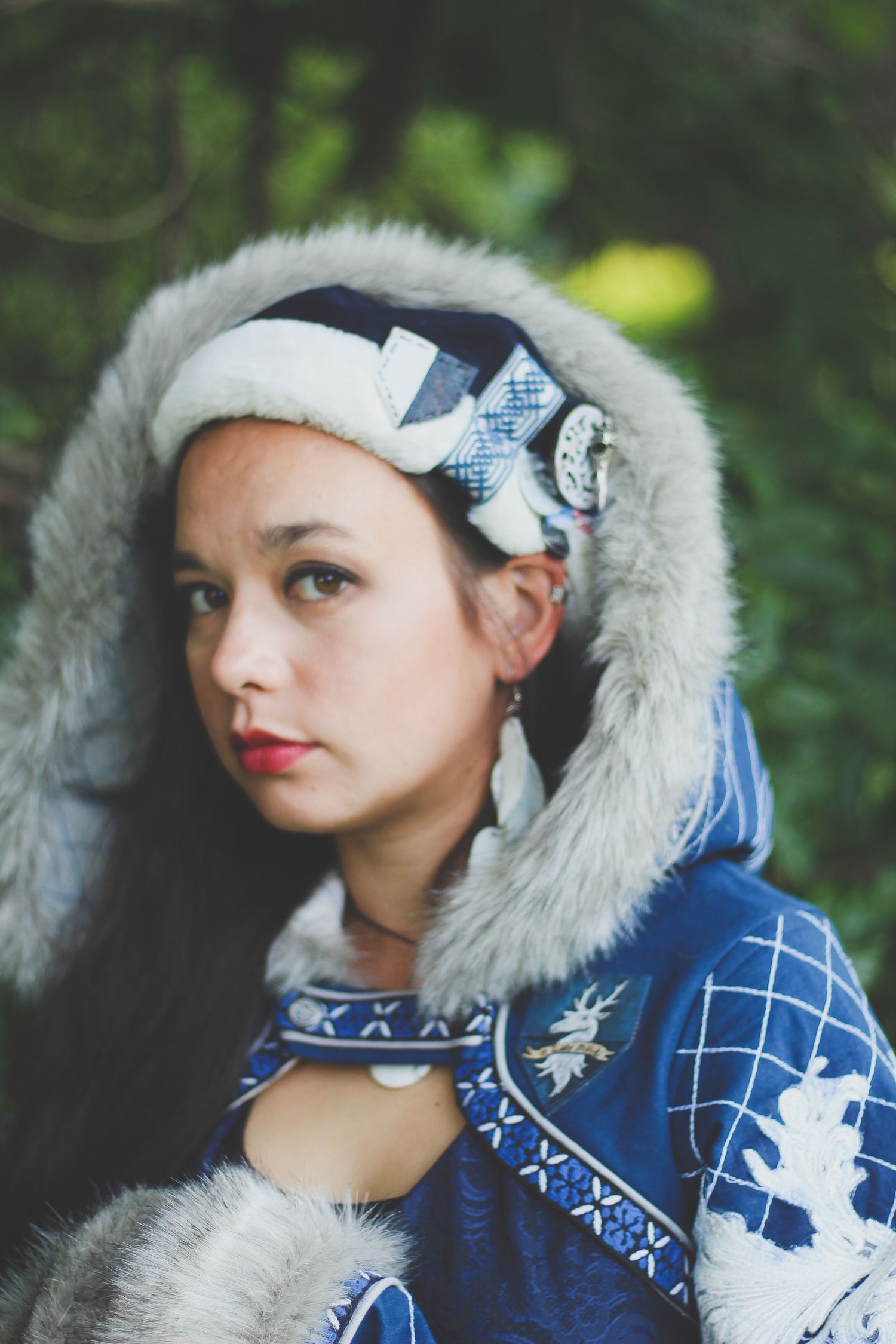 A person wearing a blue and white winter coat with fur trim and a headband poses against a blurred green background.
