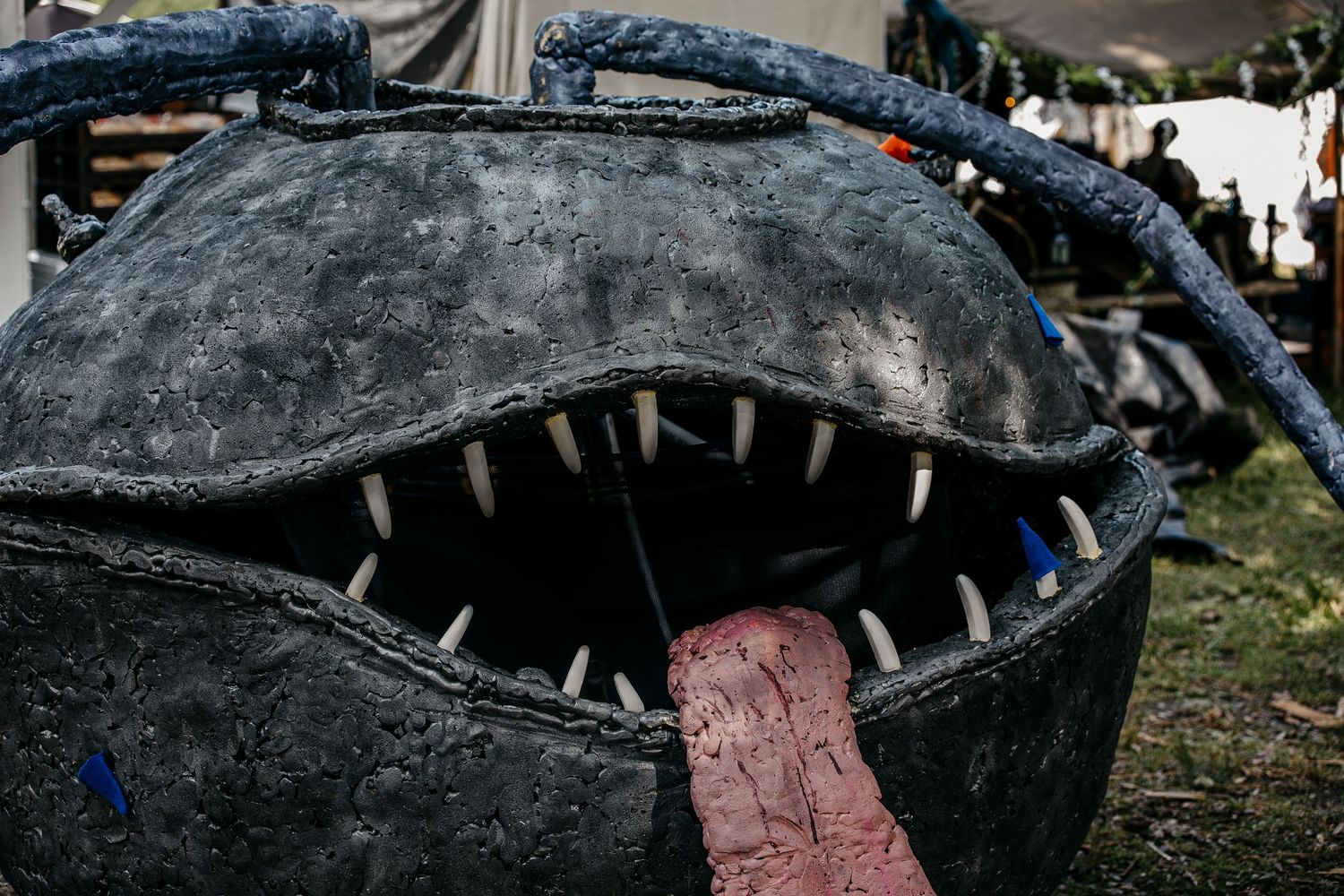 A large dark monster fish sculpture with sharp white teeth and a pink tongue on display outdoors.
