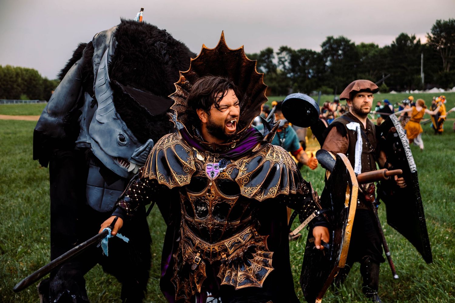 Medieval reenactors engage in battle with swords and shields on a grassy field during a historical combat event.