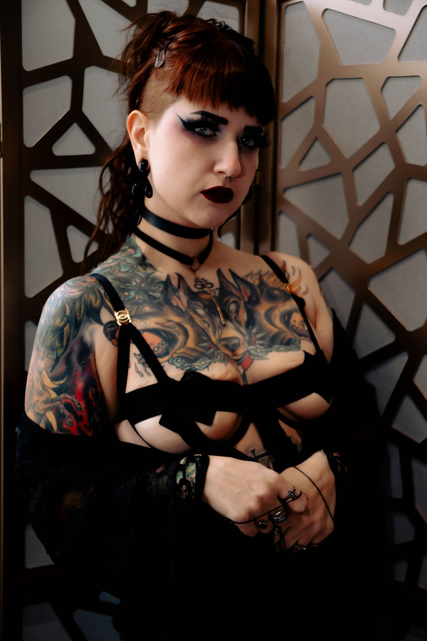 Gothic aesthetic portrait featuring dark makeup, tattoos, and choker necklace against geometric patterned background.
