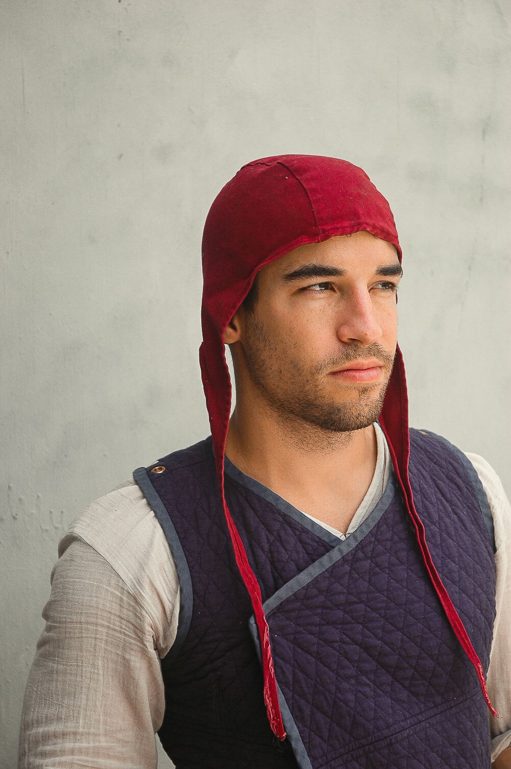 A person wearing a red cap and navy quilted vest poses against a light gray background.