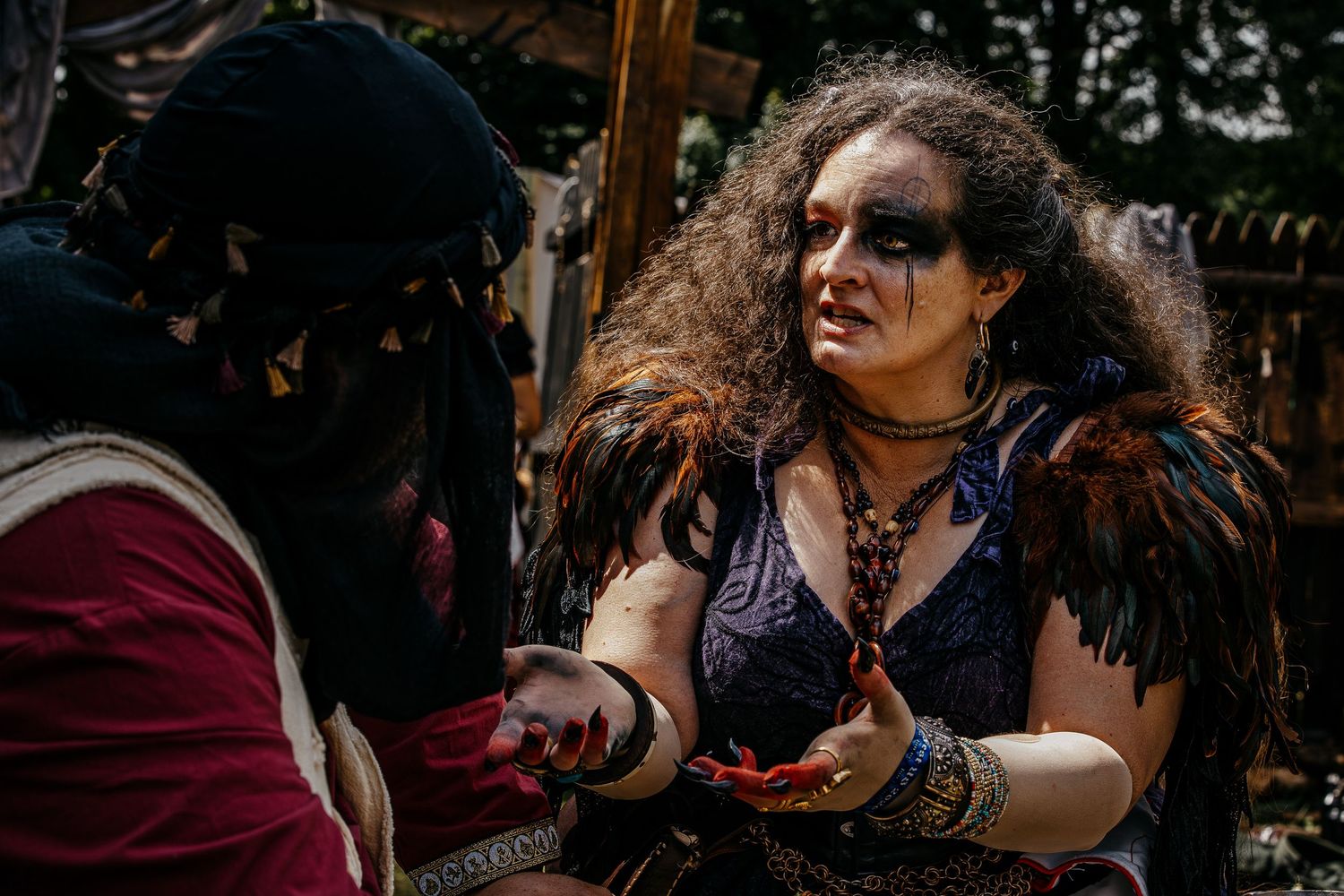 Two costumed performers in medieval fantasy attire interact dramatically at an outdoor Renaissance faire event.