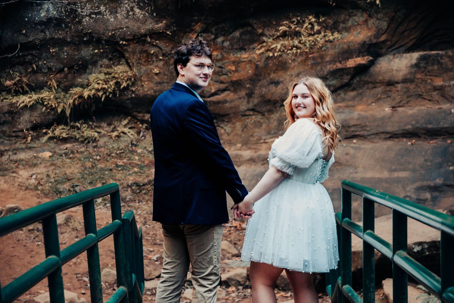 Couple walking down a green bridge while holding hands during a romantic outdoor wedding photo session.