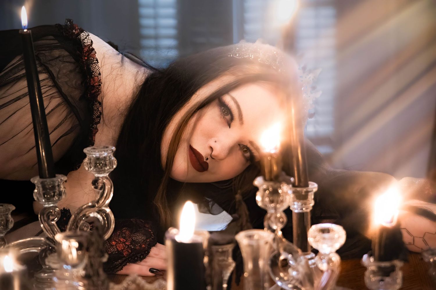 A gothic woman in black lace lies among glowing crystal candlesticks, dramatic lighting casting shadows.