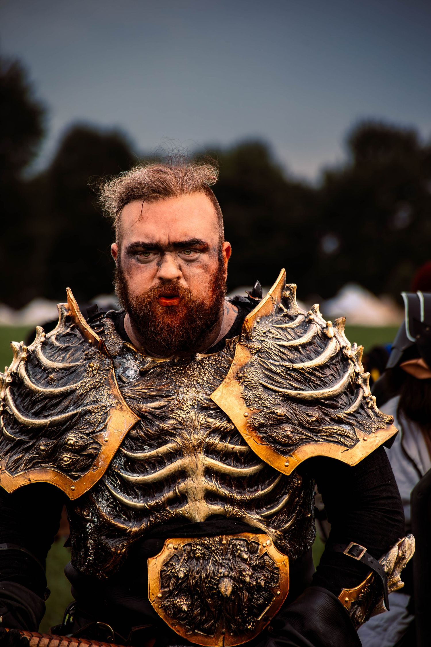 A person wearing an elaborate fantasy armor costume with metallic skeletal design and gold accents at an outdoor event.
