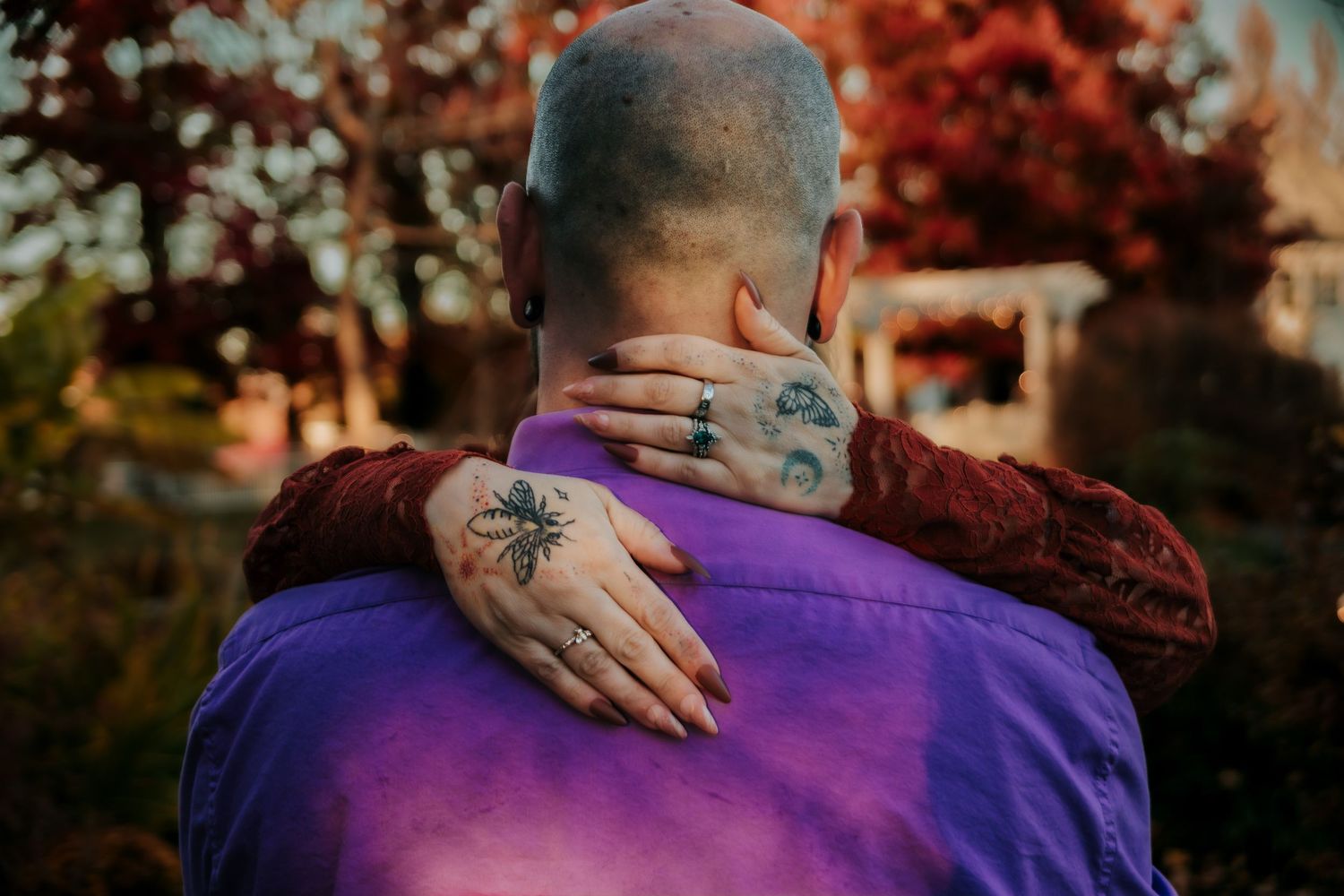 Two people embrace in an intimate moment against a backdrop of autumn foliage with vibrant purple clothing.