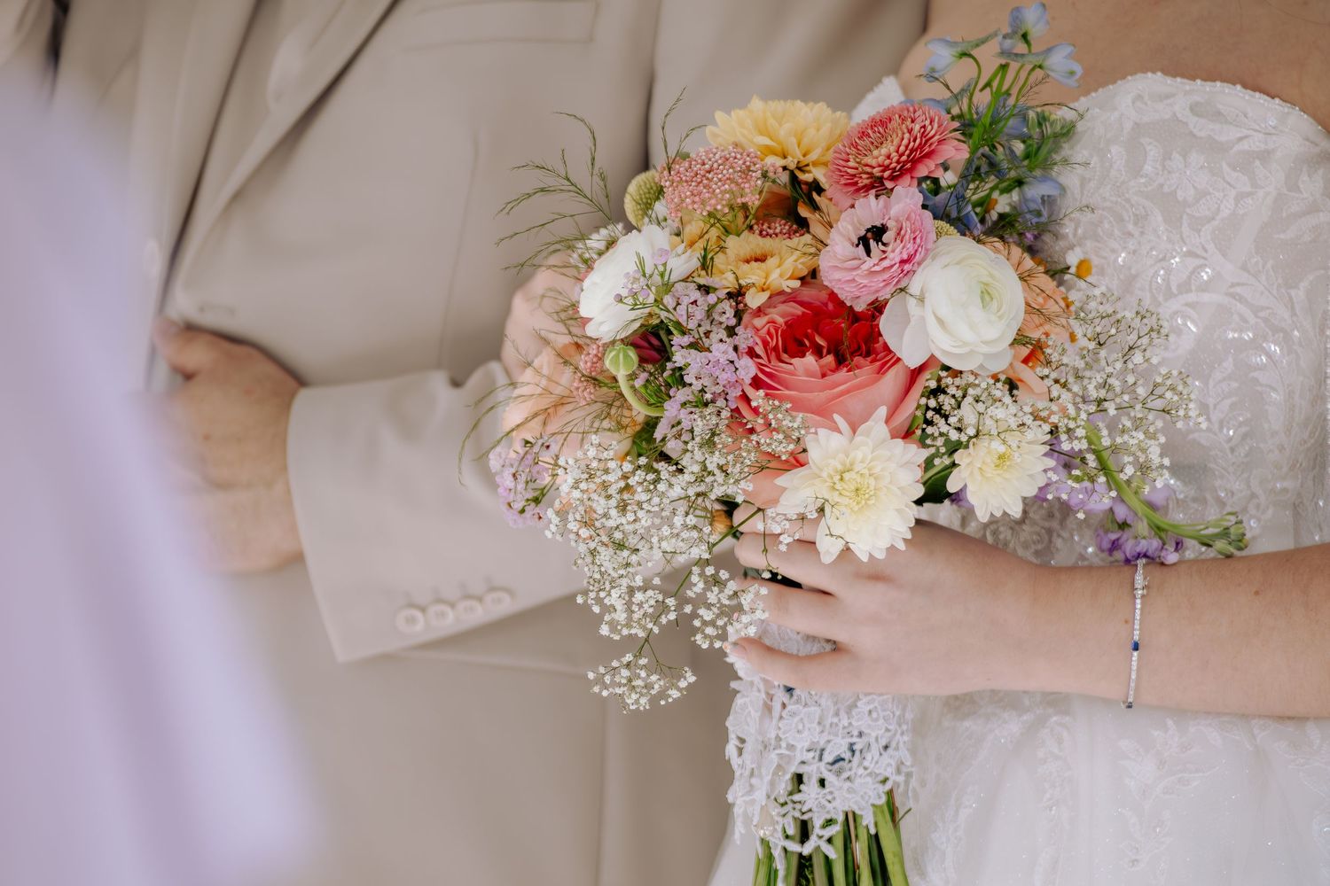 A wedding bouquet featuring pink and white roses with delicate baby's breath flowers held against a light beige background.
