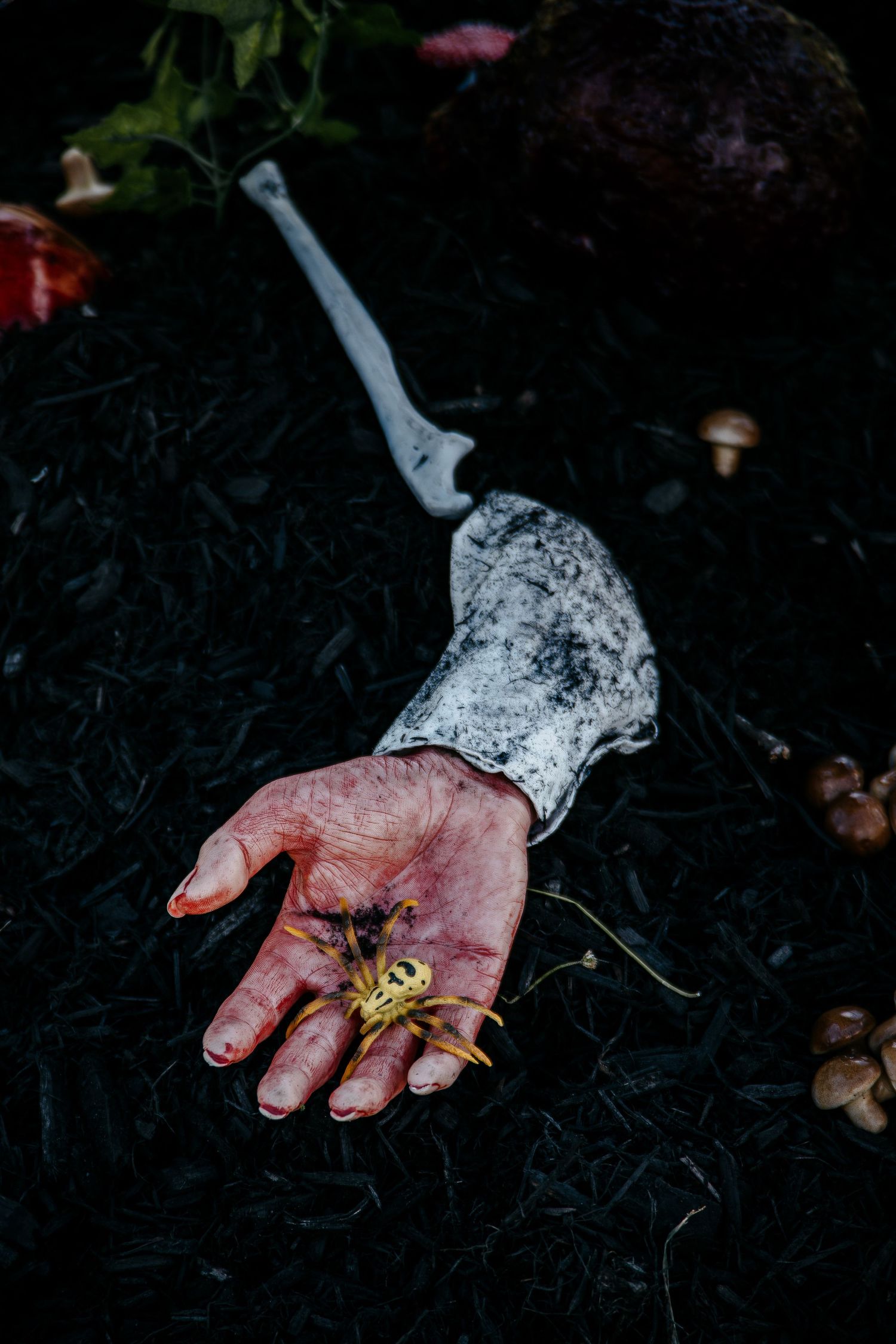 A severed hand holding a yellow flower lies on dark ground beside a skeleton arm in a Halloween scene.