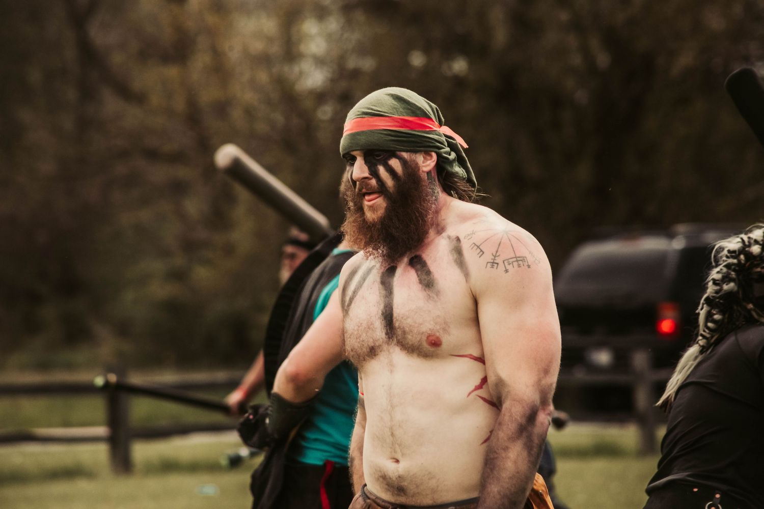 Shirtless medieval combat participants engaged in outdoor battle scene.