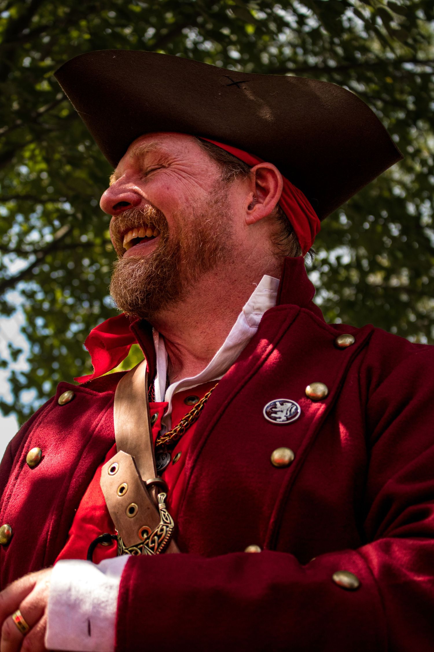 Person wearing a red colonial uniform with brass buttons smiles during a historical reenactment.