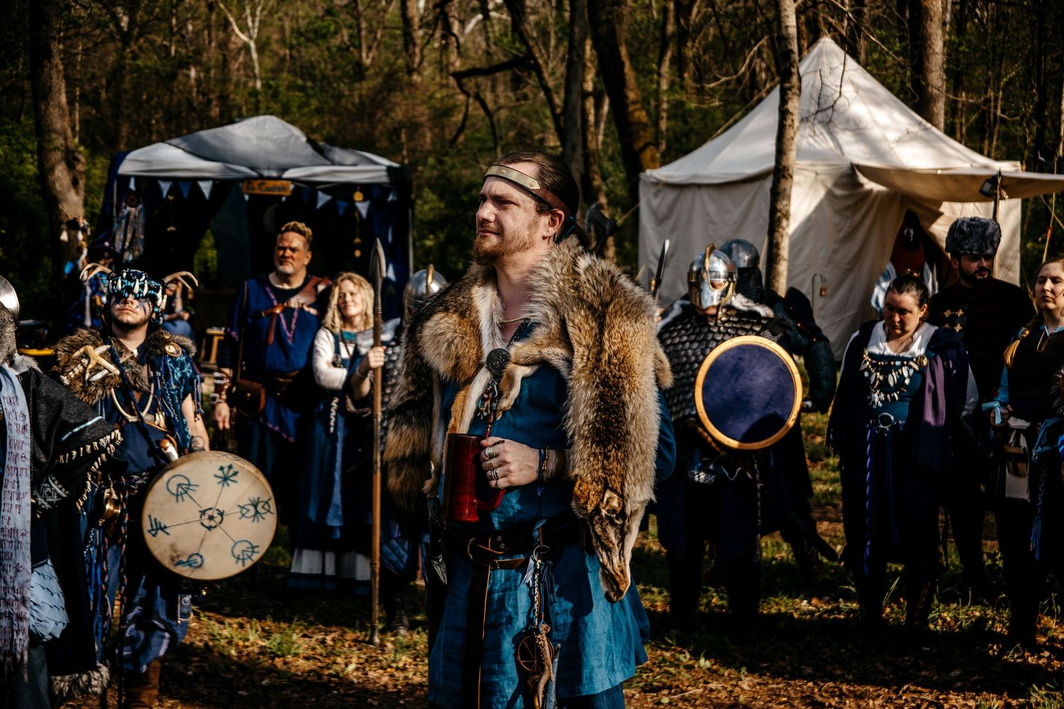 Medieval LARP event with costumed participants in Viking attire holding shields in a forest campsite.