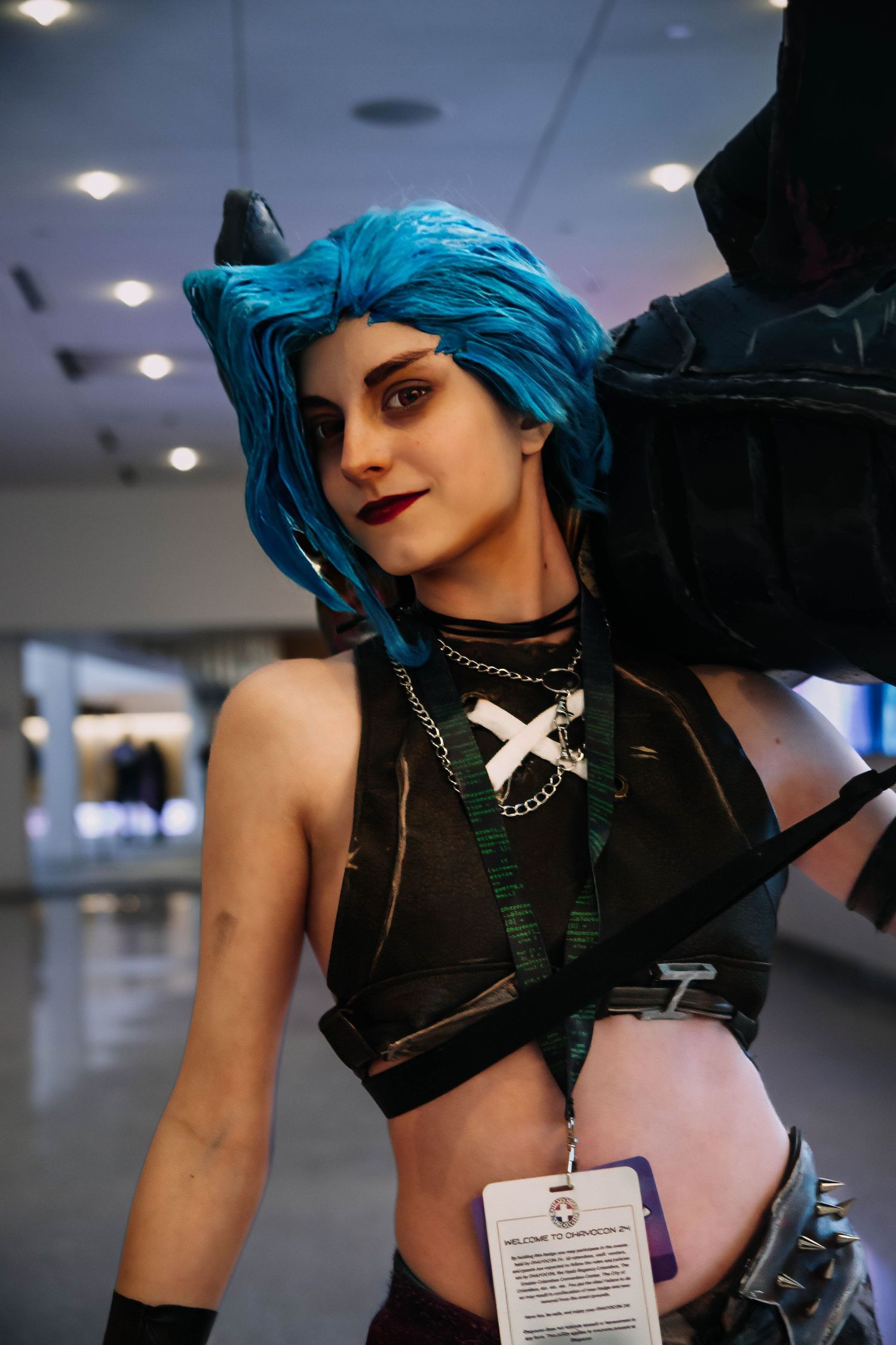 Woman cosplaying as Jinx from League of Legends with blue hair, dark makeup, and costume at a convention.