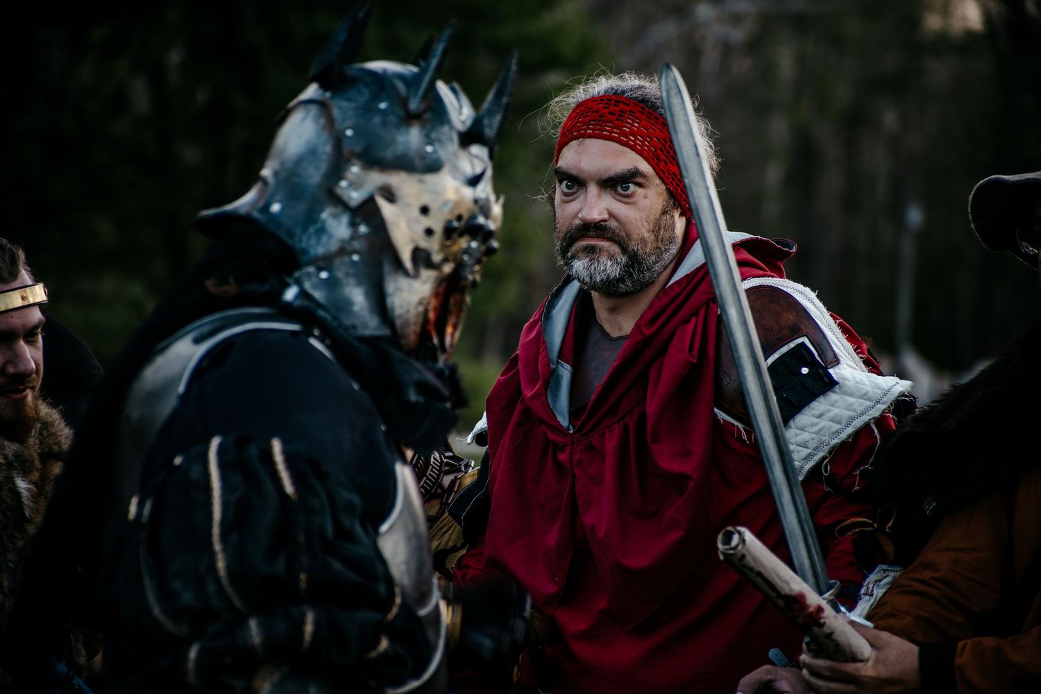 Medieval warrior in red cloak faces armored demon knight in forest battle scene from fantasy film.