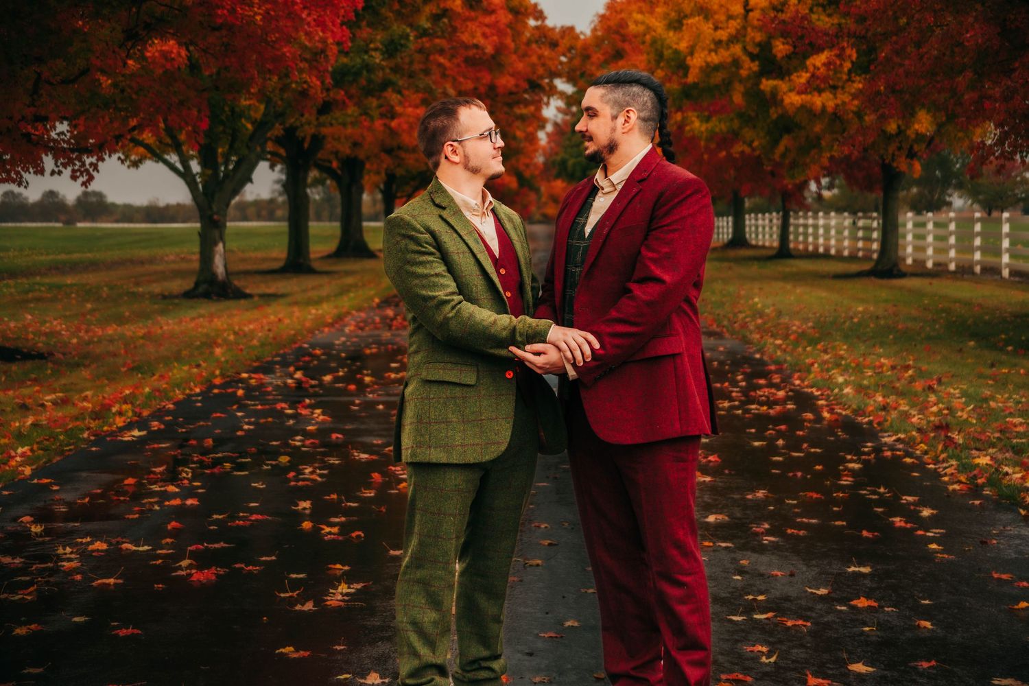 A couple shares a romantic moment surrounded by vibrant autumn foliage and fallen leaves in a park setting.