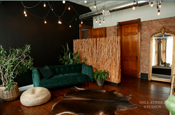 Modern living room with emerald green velvet sofa, bamboo wall divider, and string lights in a loft-style space.