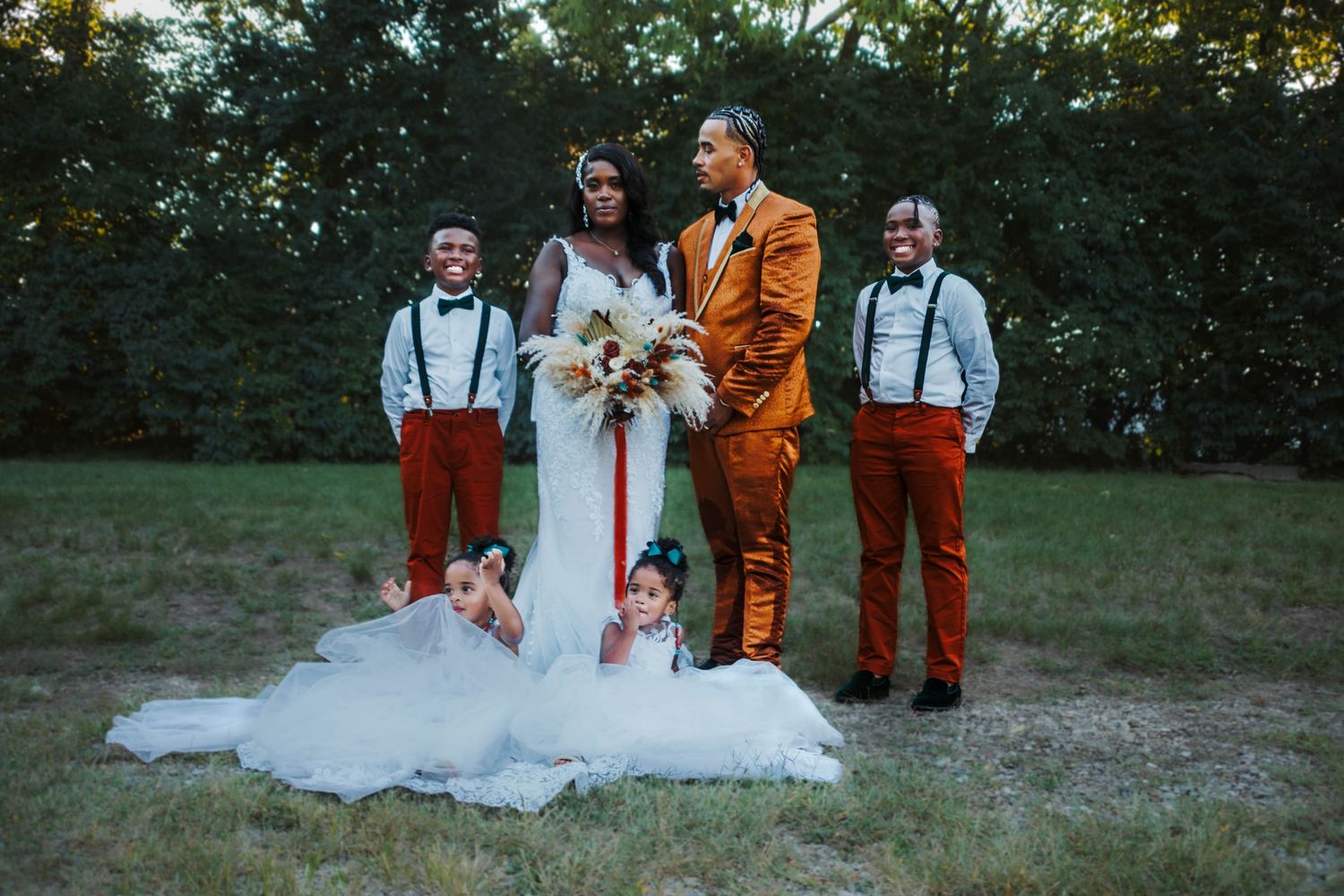 A wedding party poses together outdoors in a mix of traditional white and rustic orange attire during a fall celebration.