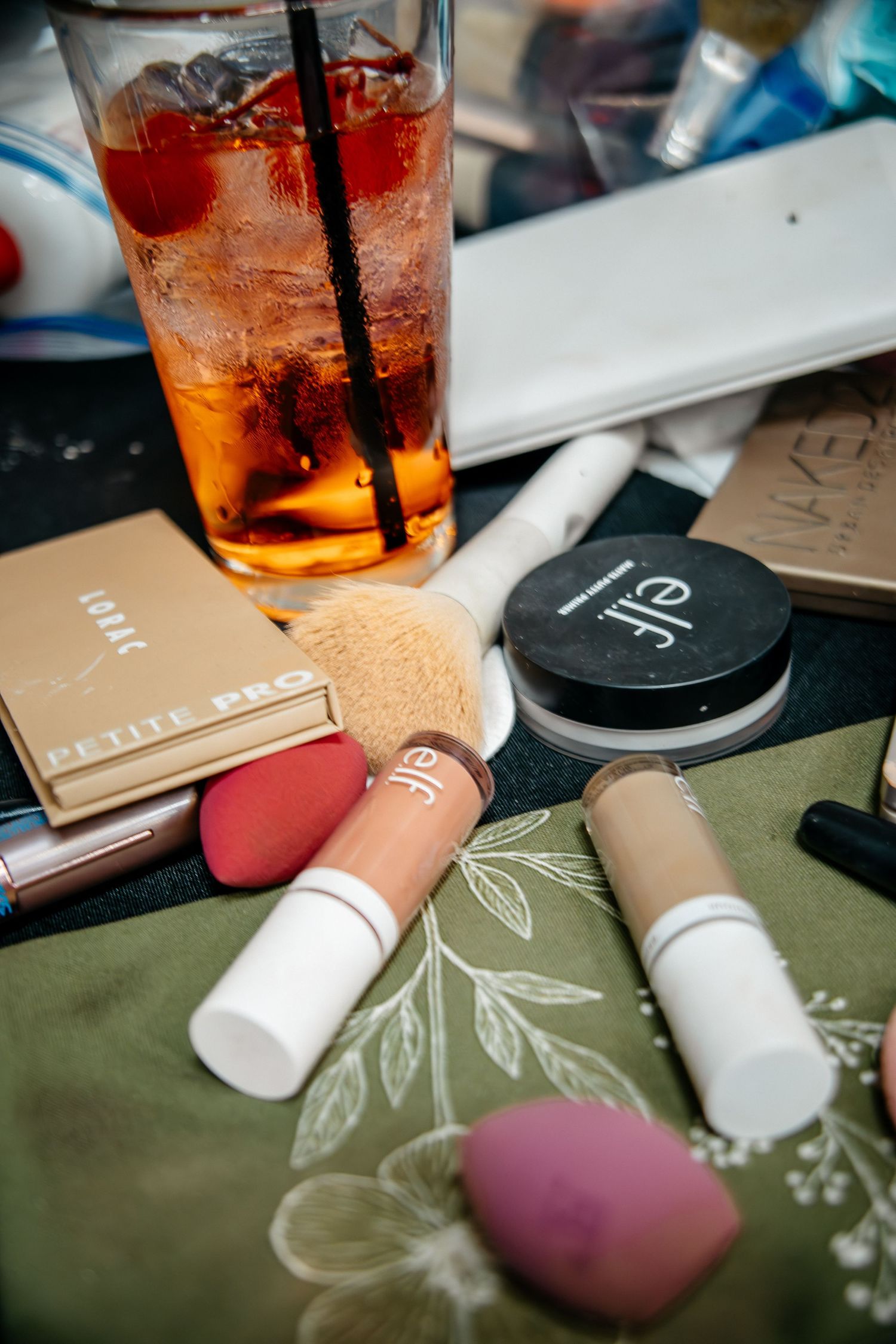 A refreshing cocktail with makeup products and beauty blenders scattered on a floral patterned surface.
