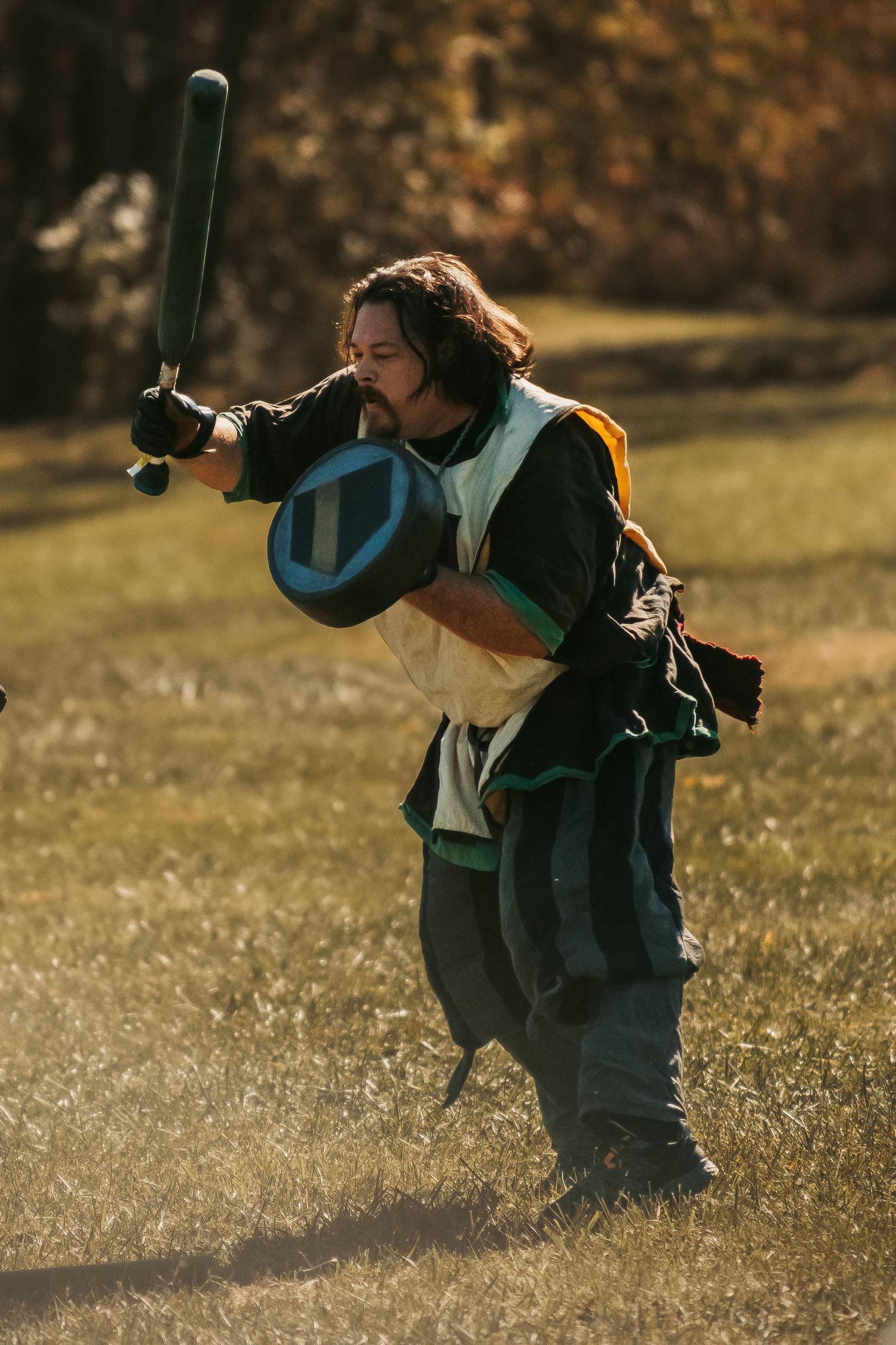 Figure in green medieval garb practicing combat moves at sunset.