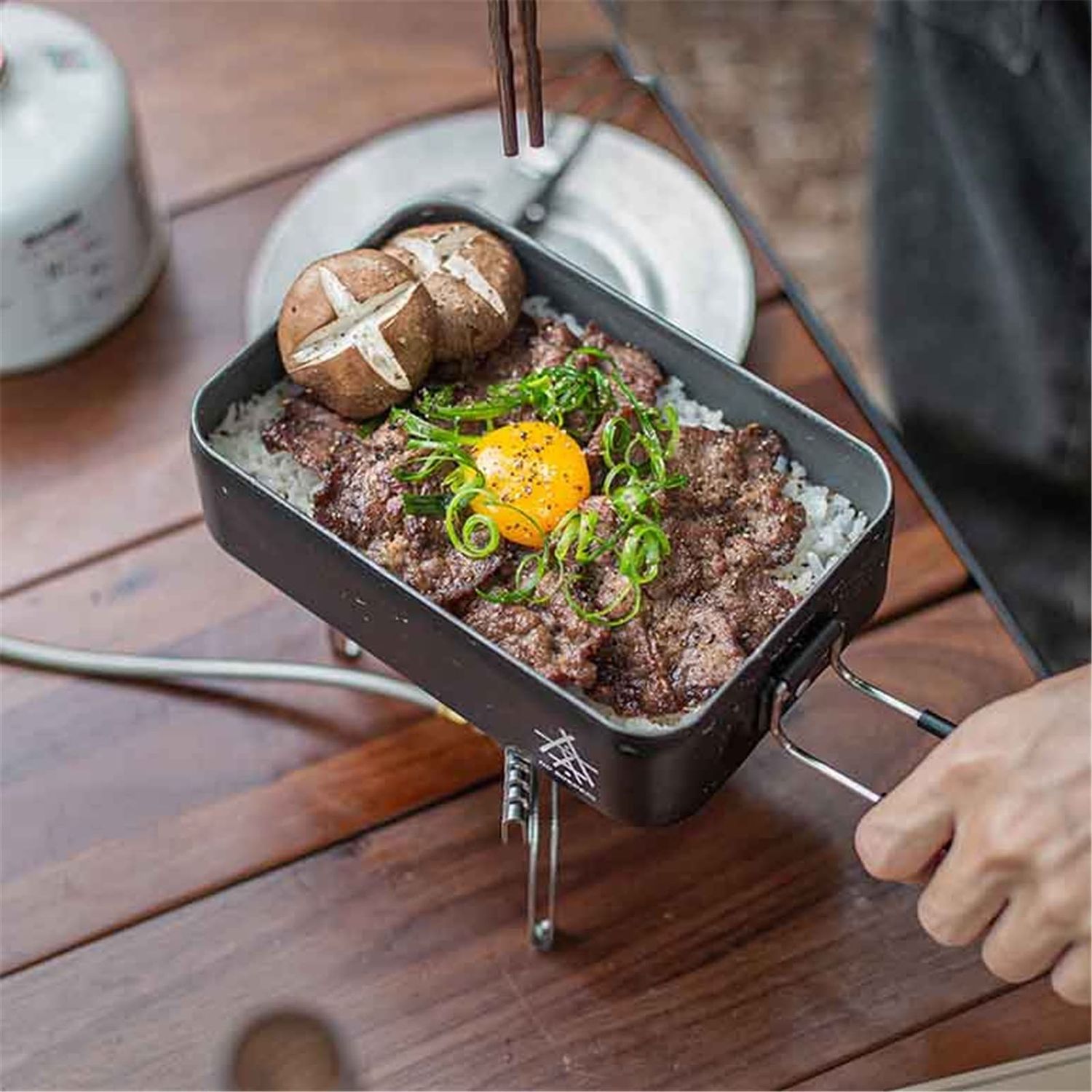 A Japanese beef bowl served in a black rectangular dish with raw egg yolk and green onions on top.