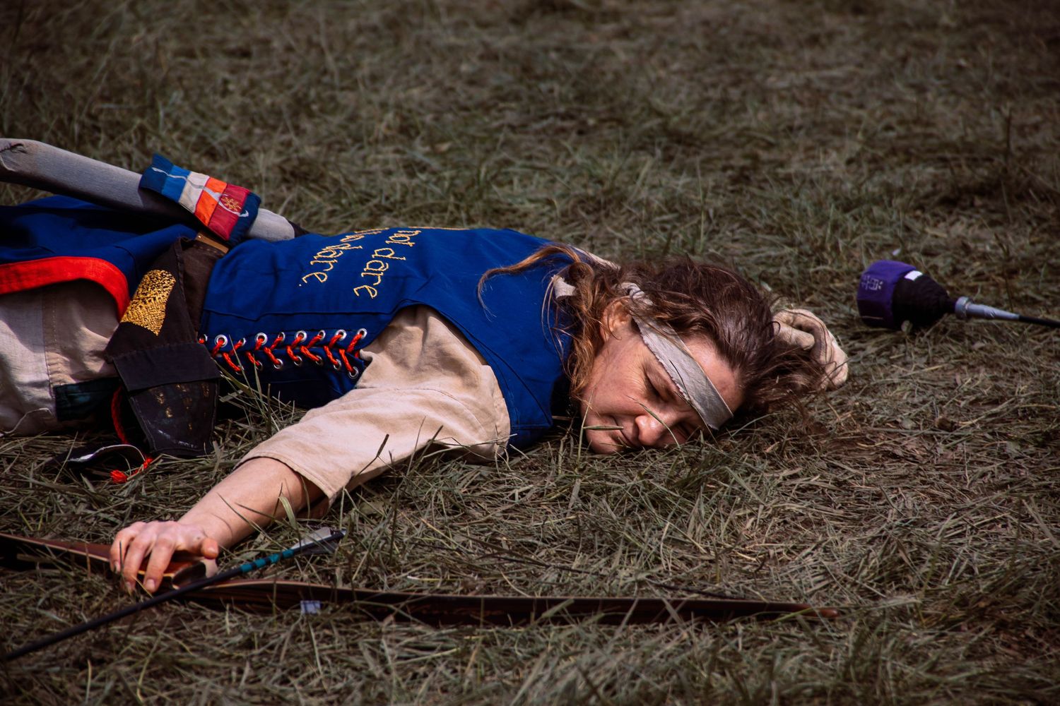 A person lies motionless on brown grass wearing blue and red athletic clothing.