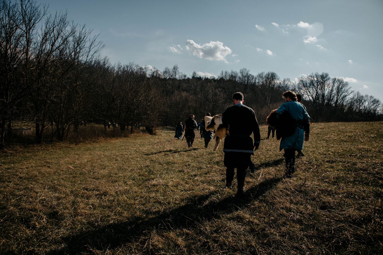 A group of silhouetted figures walk across a barren winter field under a cloudy blue sky.
